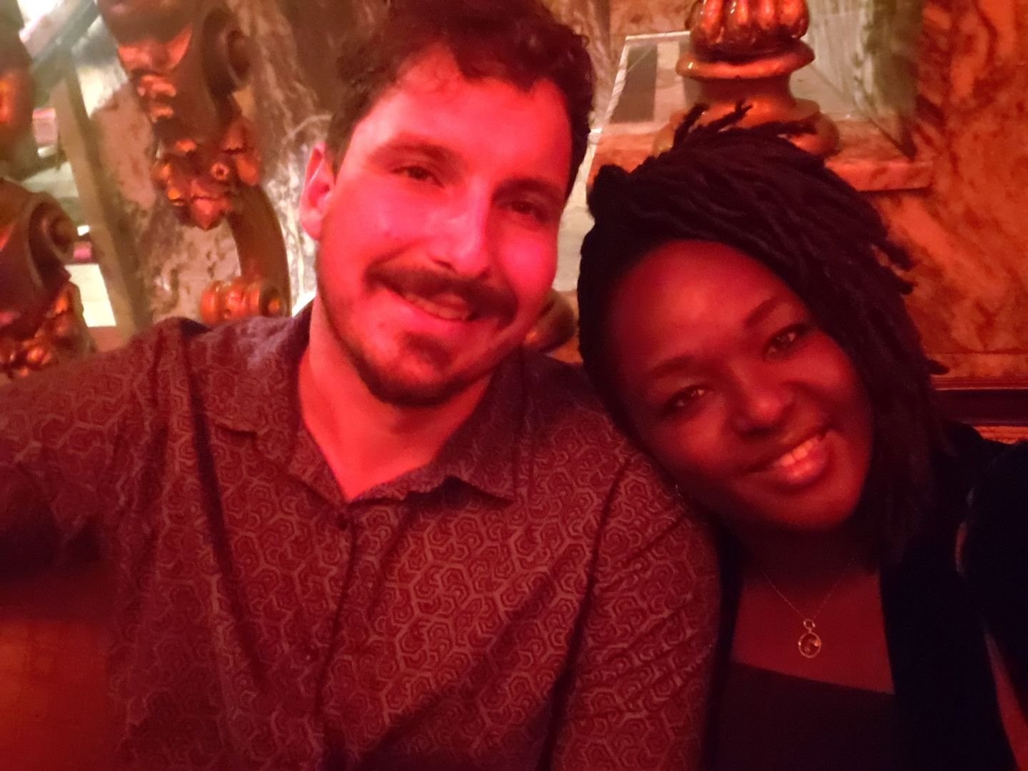 A man and woman smiling together in a warmly lit setting with ornate decorations in the background.