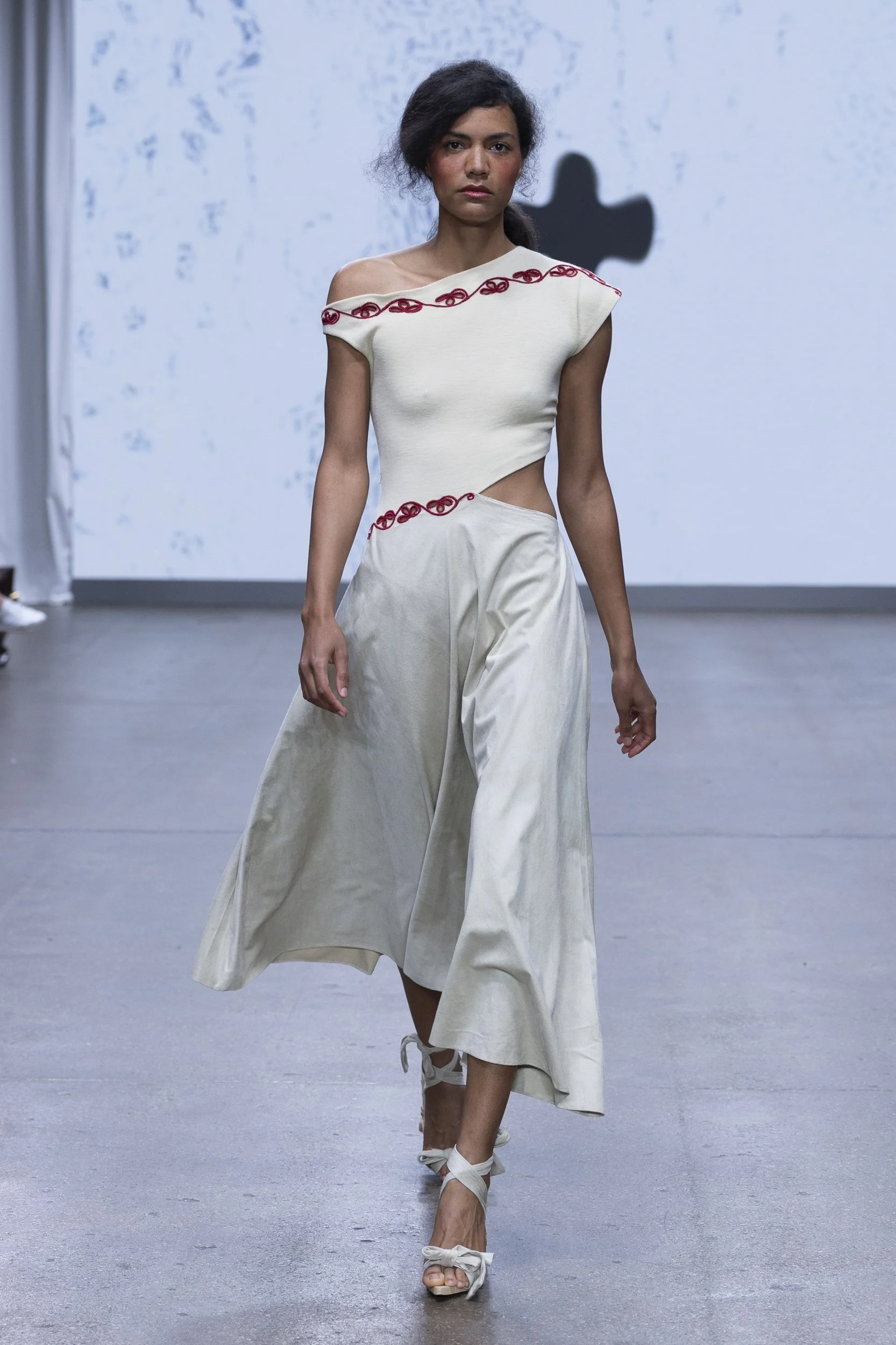 Model in an off-shoulder ivory dress with red embroidered detail from ALISADUDAJ Silent Engravings SS26.