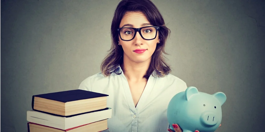 young-woman-with-stack-pile-of-books-and-piggy-bank-full-of-debt-picture-id820859898-2.jpg