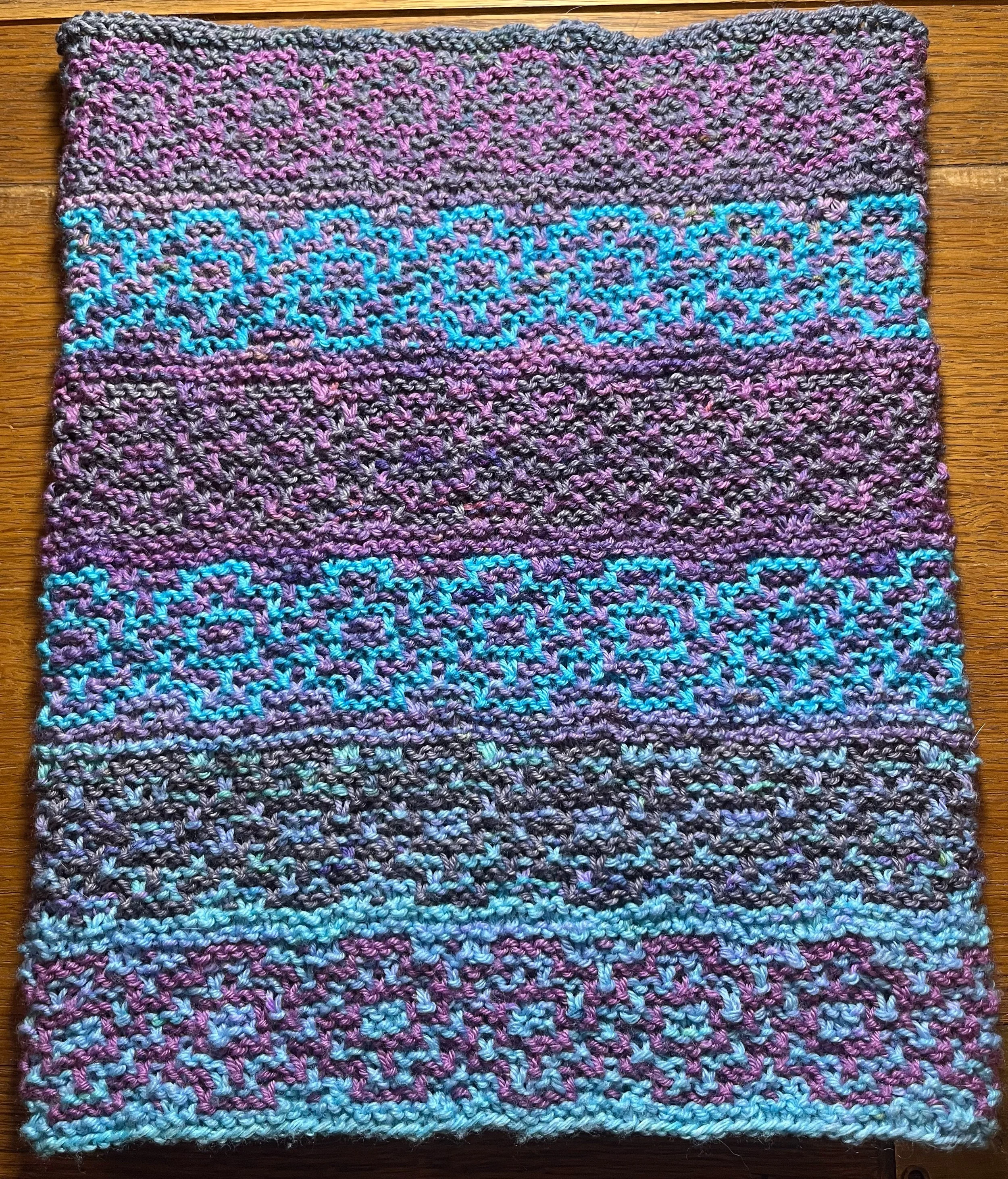 Image is of a knitted tube in purple, blue and grey. The visible pattern is geometric.