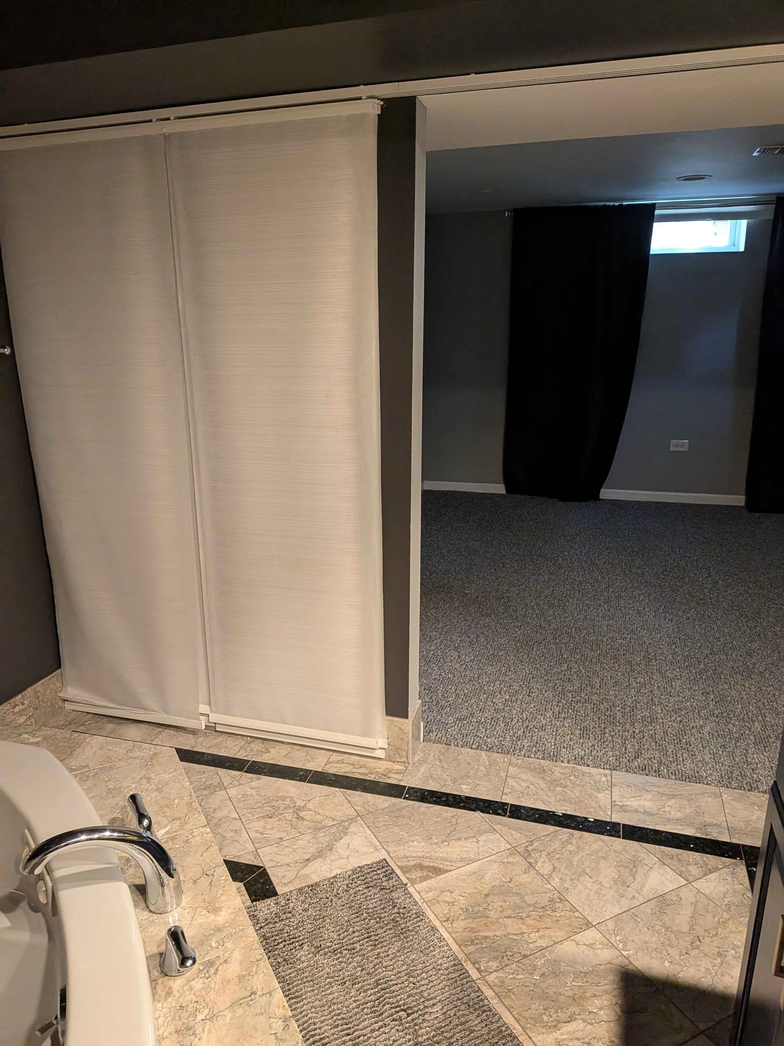 View from the bathroom into a currently empty and dark bedroom.