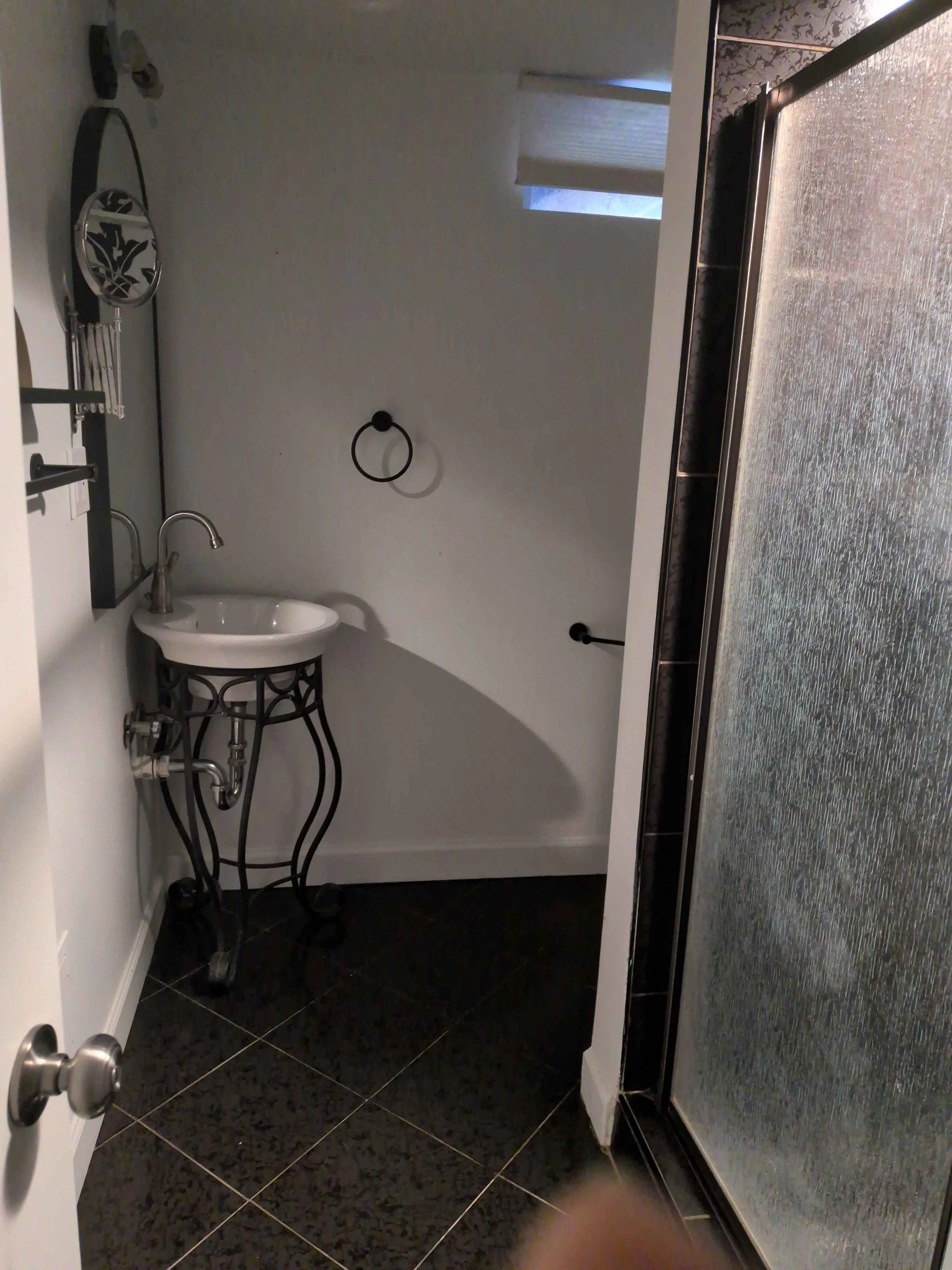 Doorway view into a bathroom. Visible is a shower door, two mirrors and a pedestal sink.