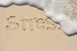 THe word stress written in sand being washed away by waves.