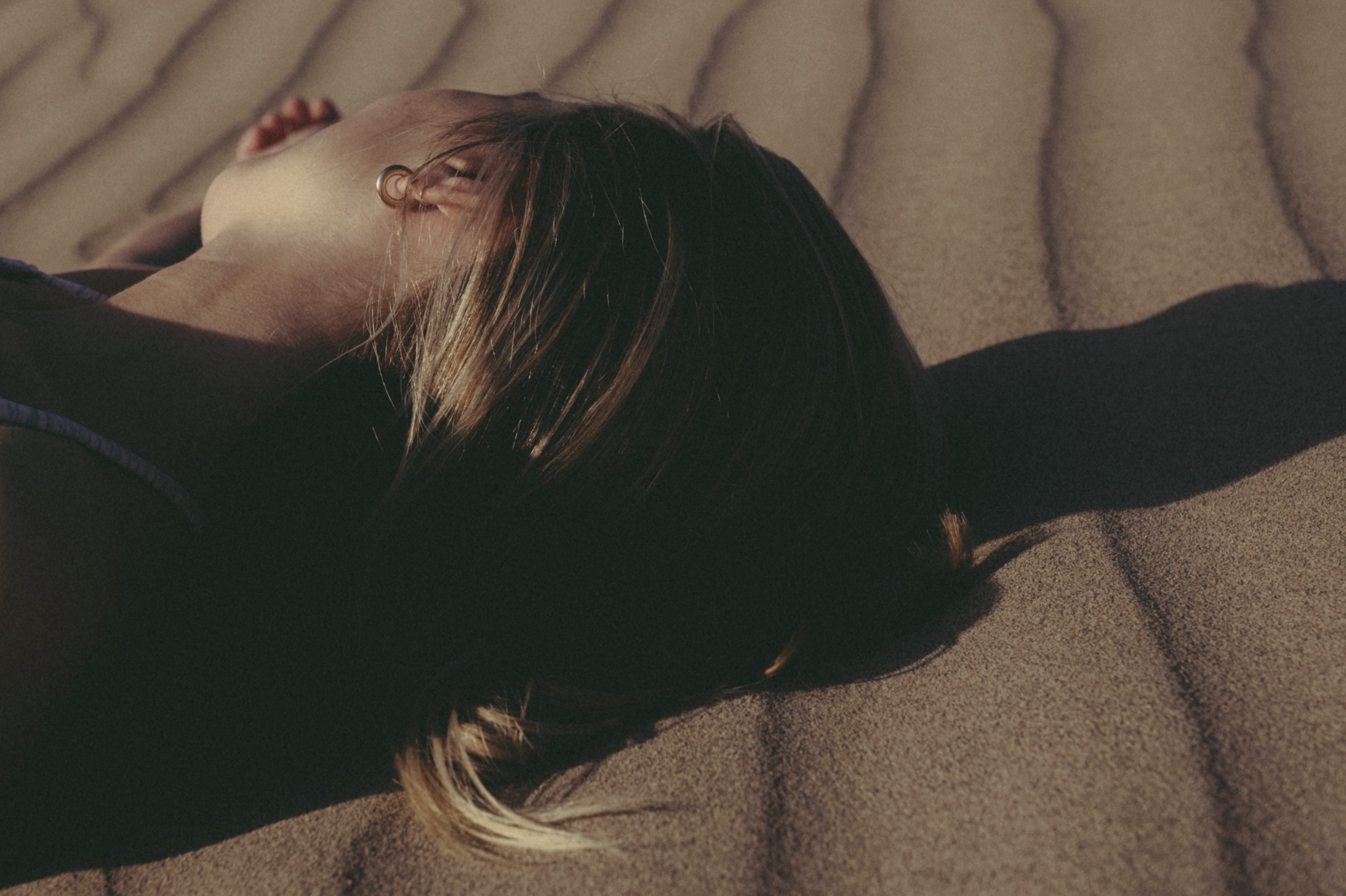 A person lying on the ground outdoors, with shadows and sunlight highlighting their hair and face.