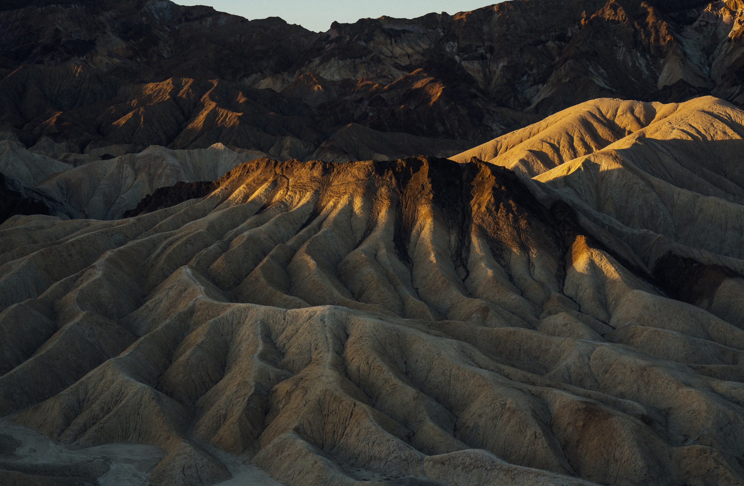 Sunlit rugged desert mountains with layered, multicolored geological formations.