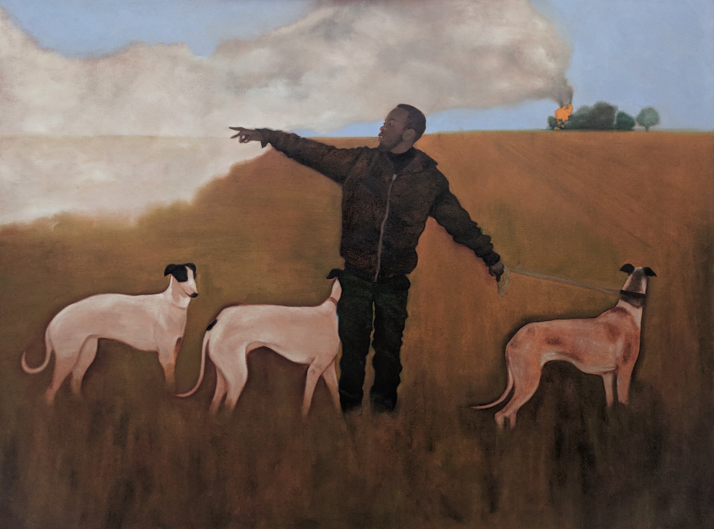 A man in a black jacket and pants is pointing to the left and holding a leash attached to three dogs, standing in a grassy field with a cloudy sky and smoke pluming from a fire in the background.