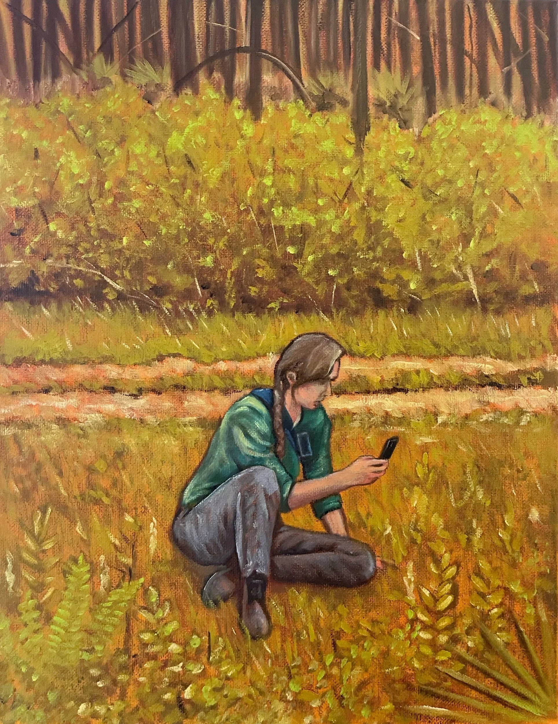 A woman with braided hair wearing a green jacket and gray pants sitting on the ground in a field, looking at her phone with trees and foliage in the background.