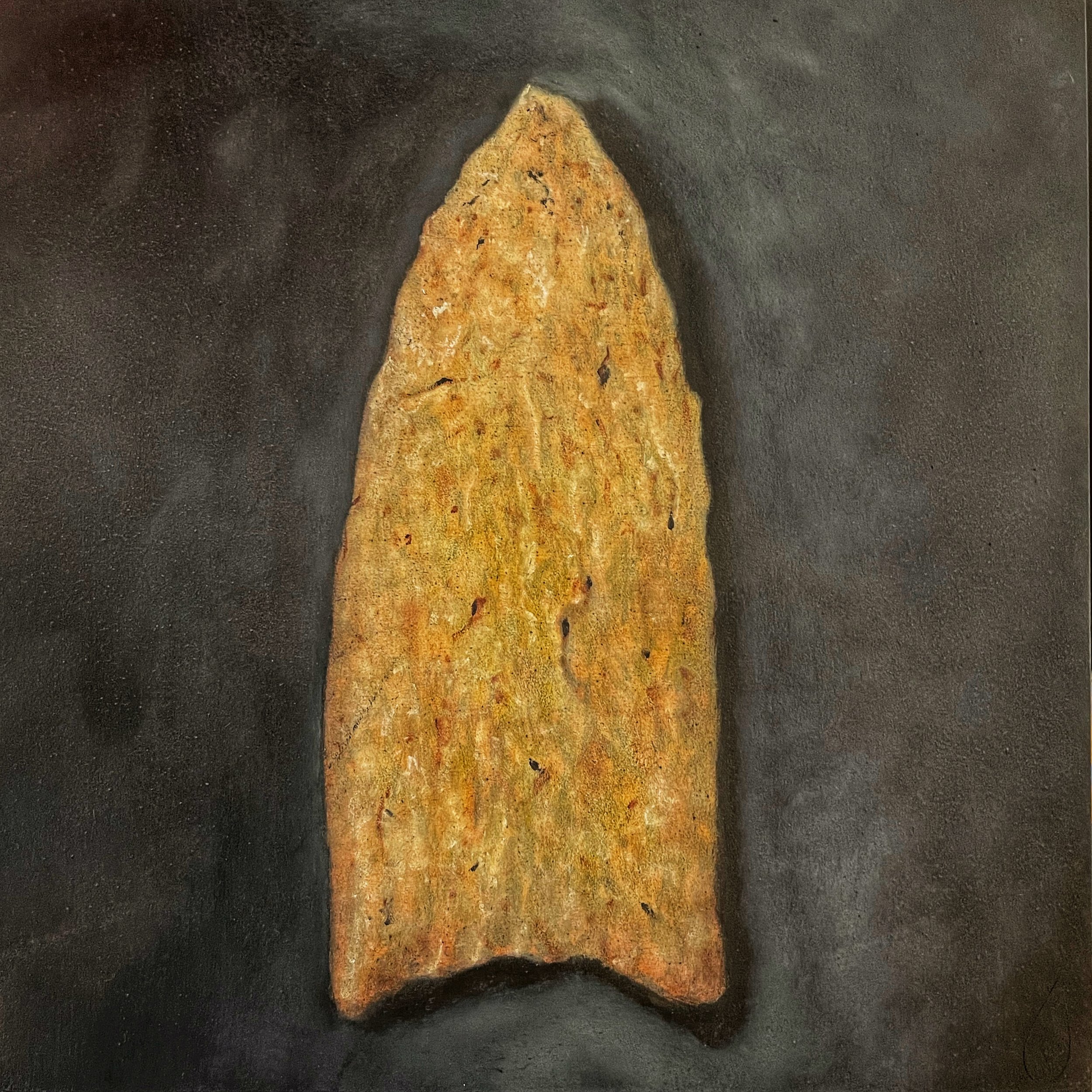 A prehistoric stone arrowhead with a pointed tip and broad base, resting on a dark surface.