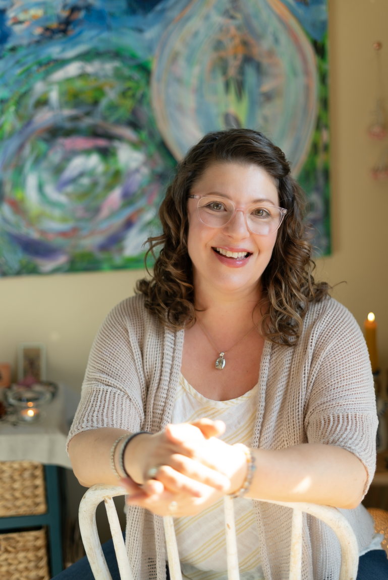Woman with brown curly hair in a light tan linen sweater sits in front of an abstract painting
