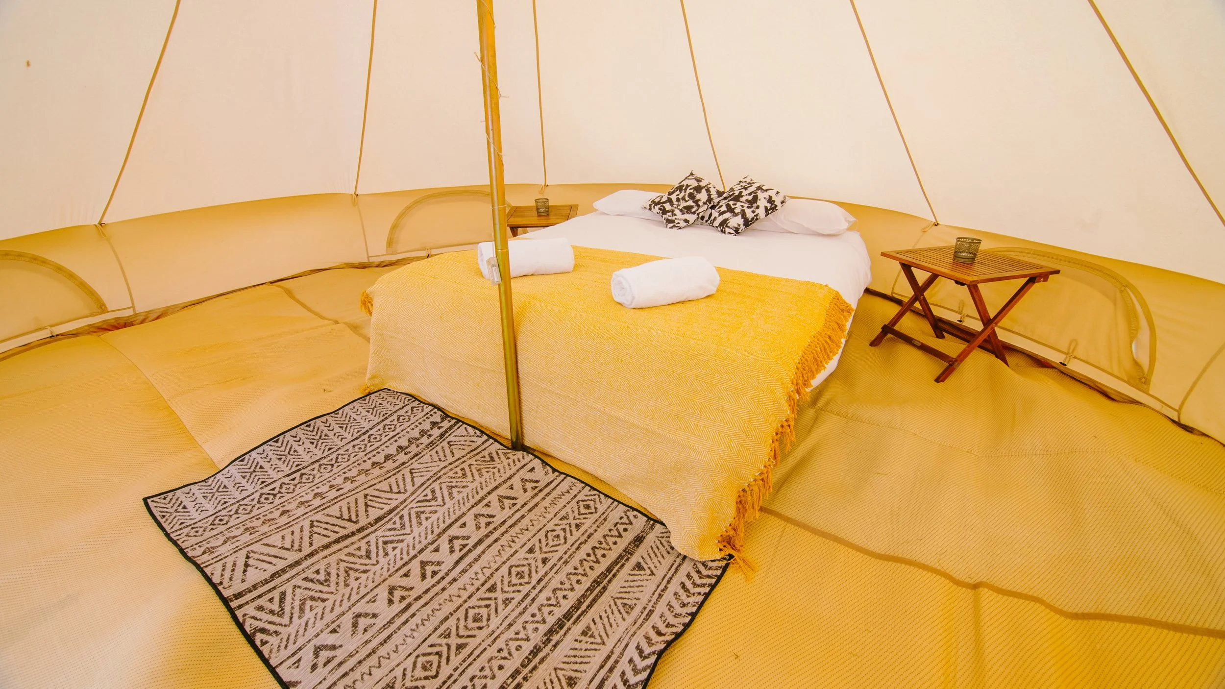 Luxury bell tent interior at Endure 24 Reading with vibrant yellow bedding, wooden furniture, textured rug, providing upgraded accommodation for endurance race participants.