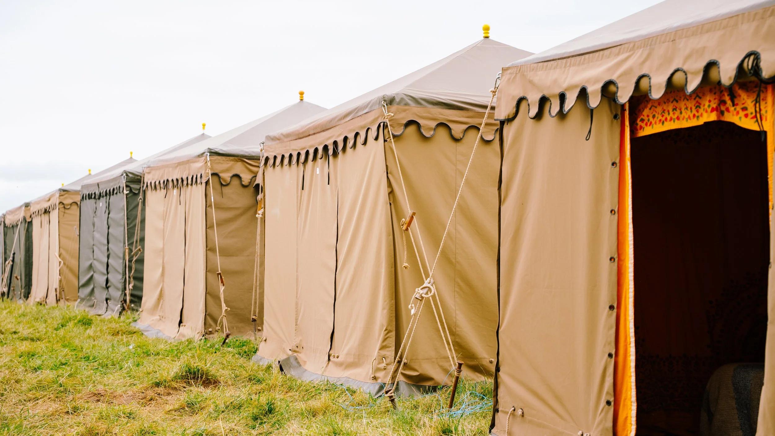 Inside a large beige camping tent with colorful bean bag chairs, a projector, and a screen for movies or presentations.