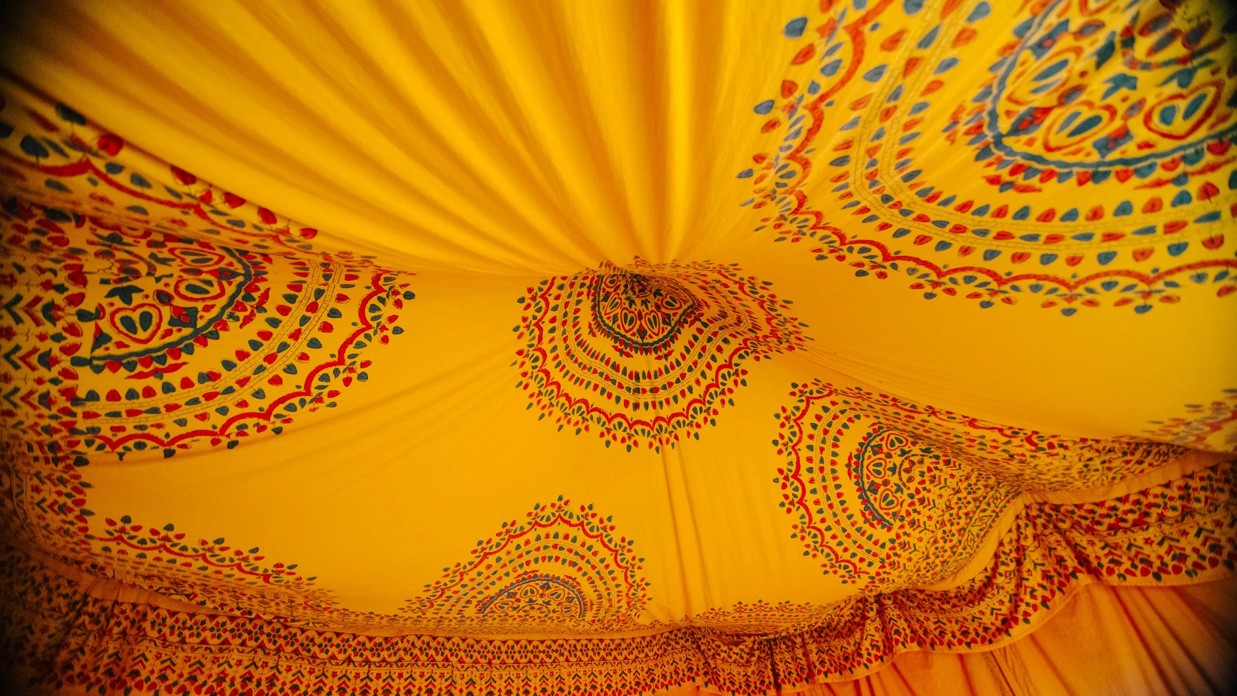 A yellow fabric or covering with intricate colorful mandala-like patterns in red, blue, and green, creating a vibrant and decorative design.