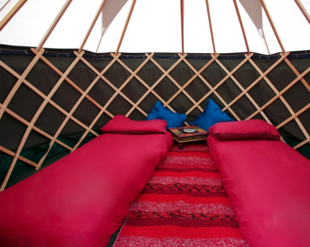 Inside a yurt with two sleeping bags, one on each side, with pillows and a book in the middle, and a red rug on the floor.