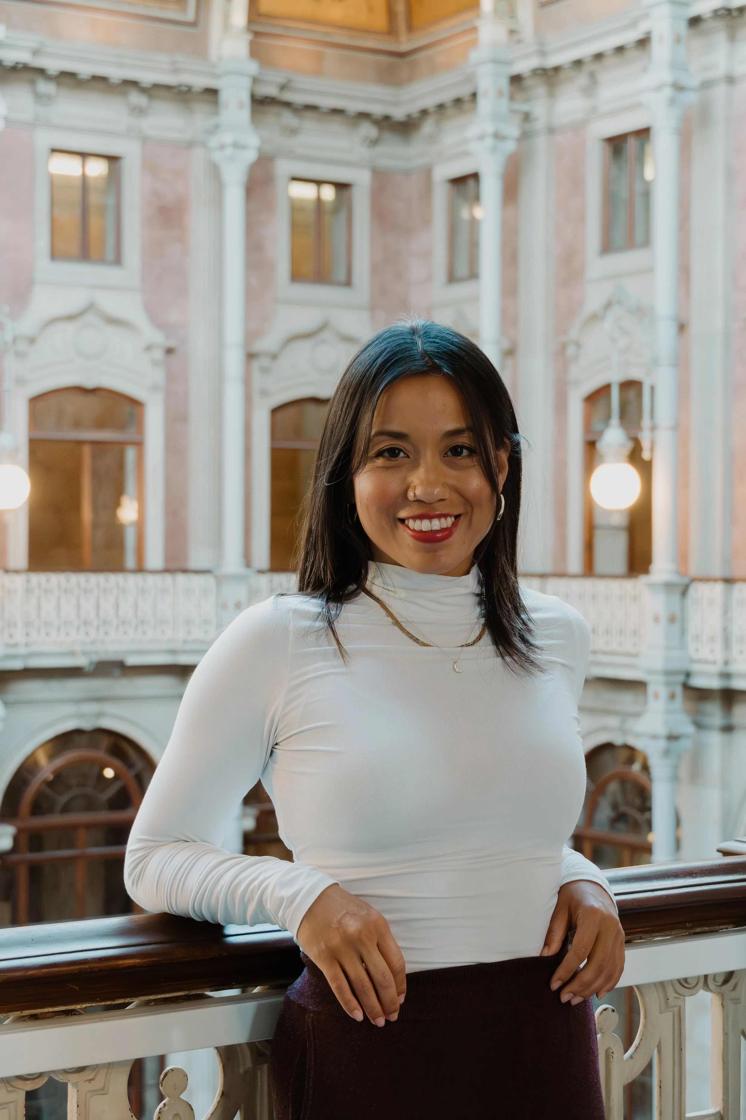 Emilie Wong, a woman of South Asian descent wearing a white turtleneck and maroon pants standing inside the ornate Palacio da Bolsa in Porto, Portugal.