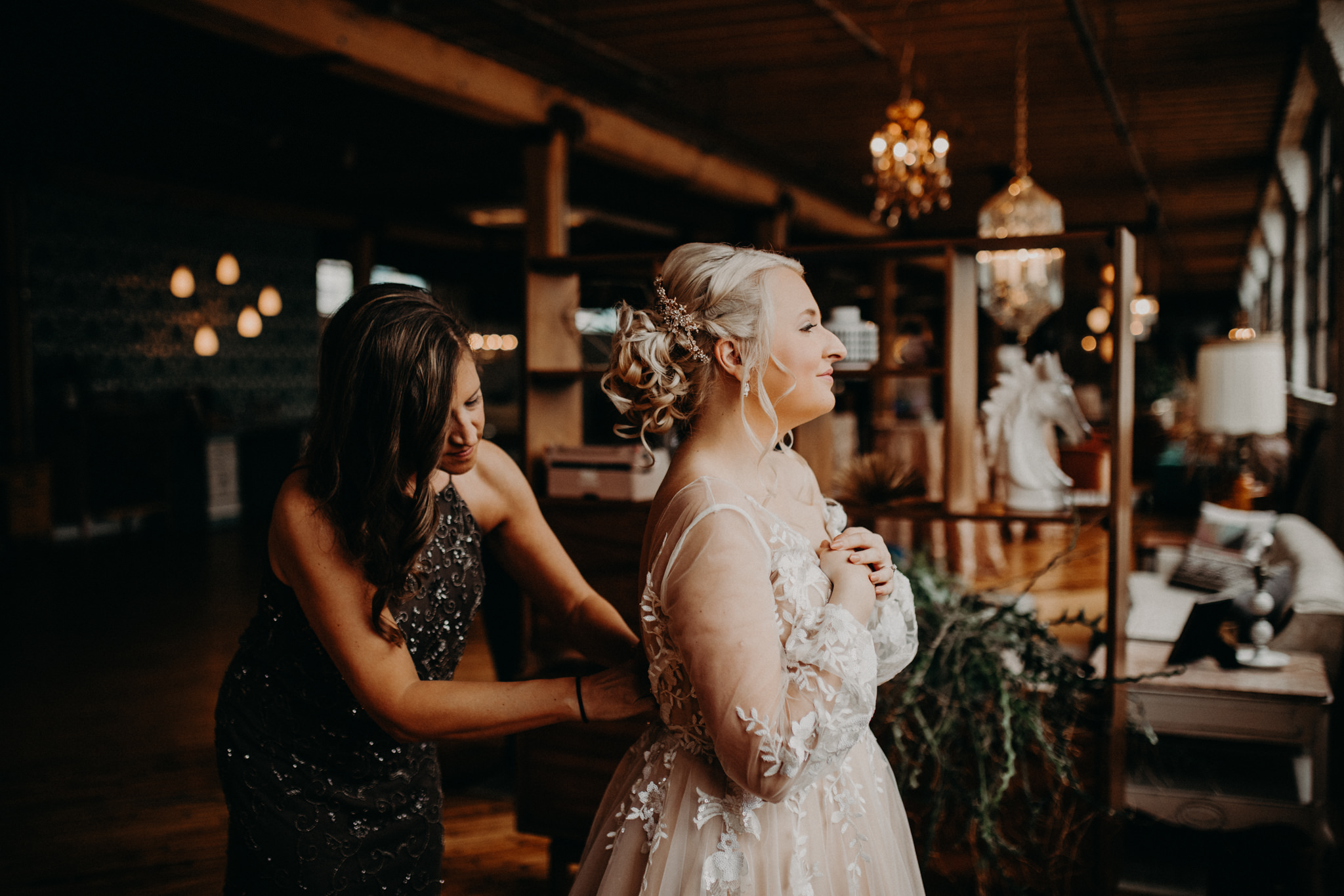 Bride being zipped up by mother in front of lights at The Cheney Place