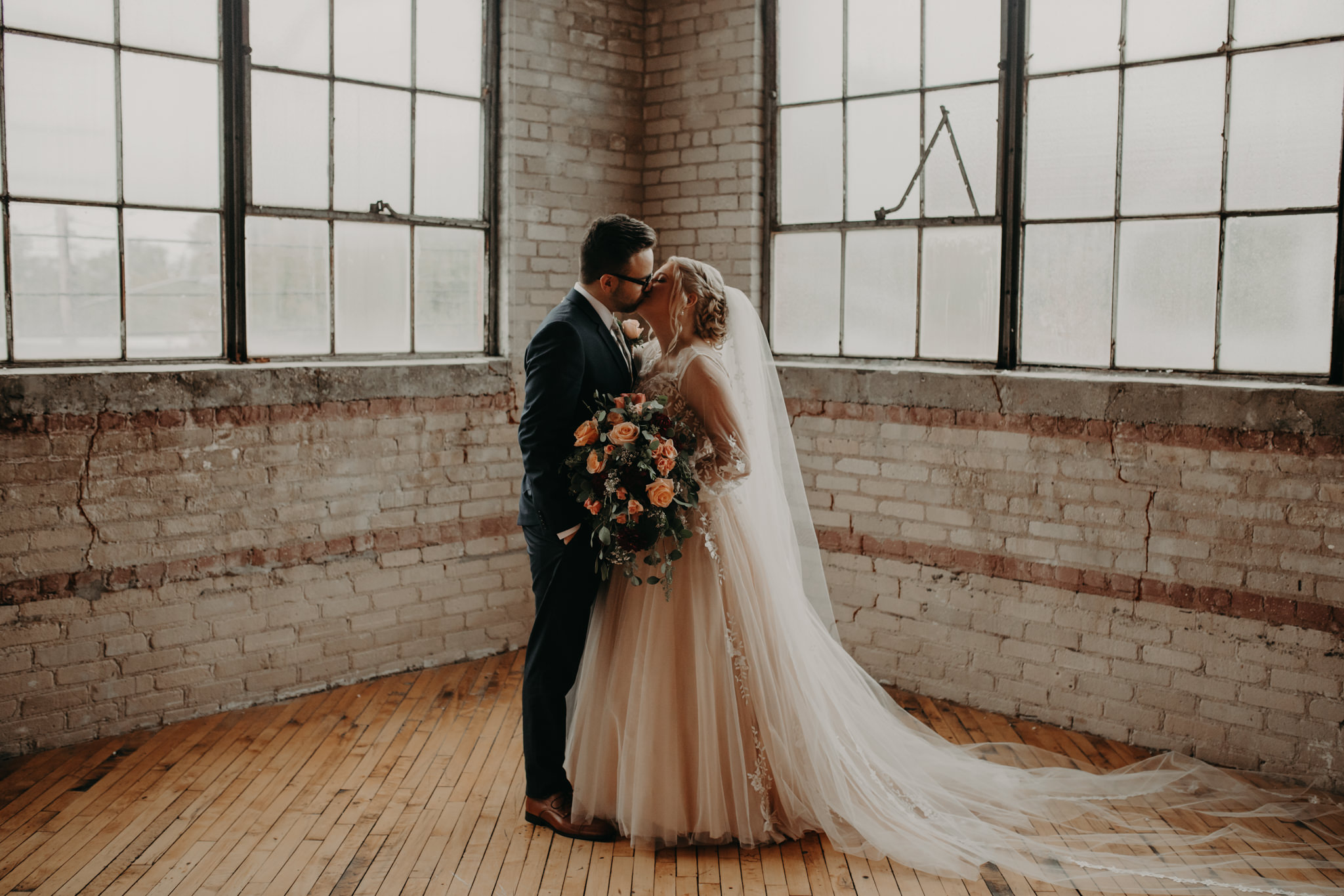 Bride and groom kissing in front of square windows and brick