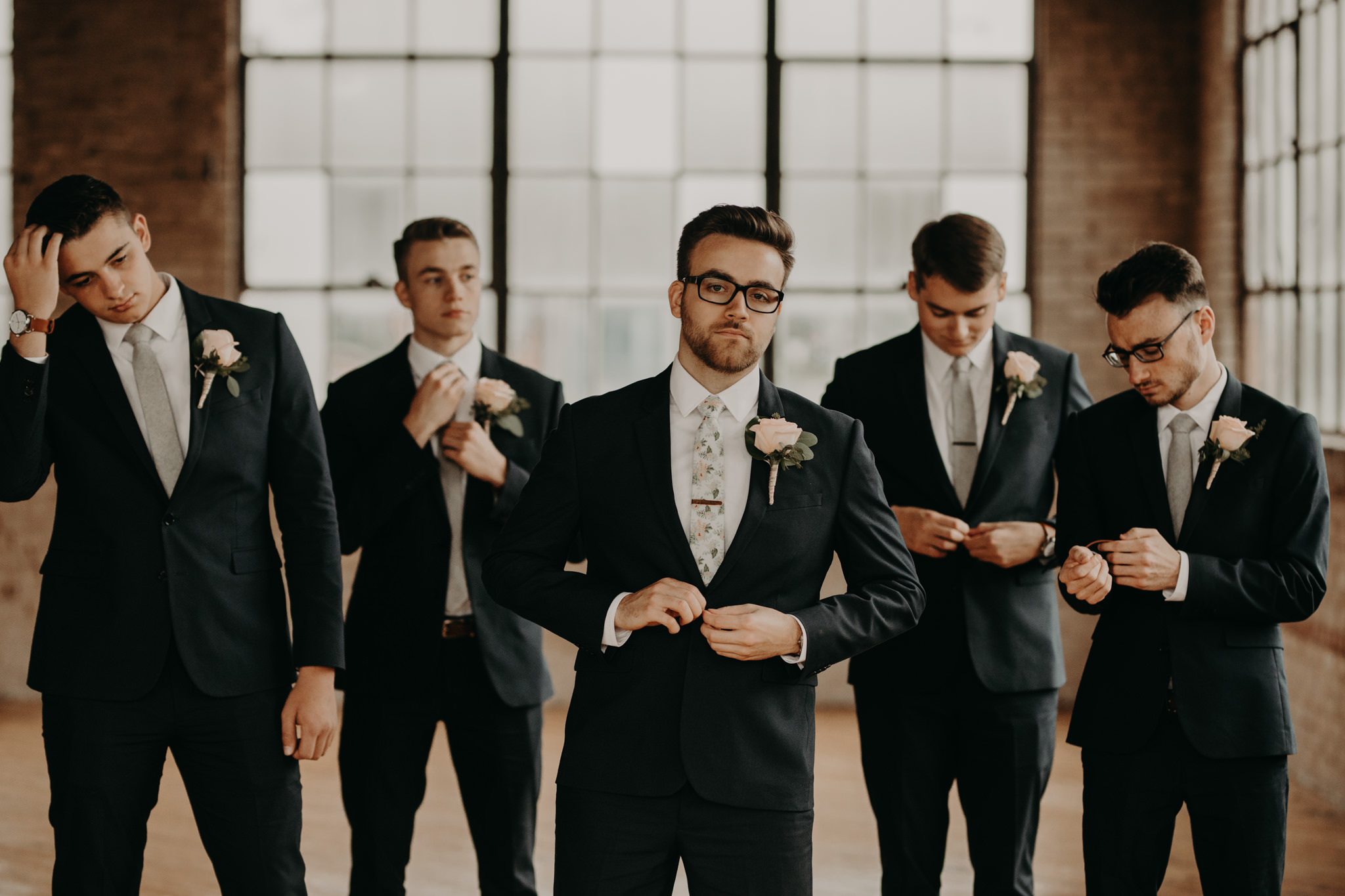 Groomsmen in navy suits and floral ties standing in front of windows and brick