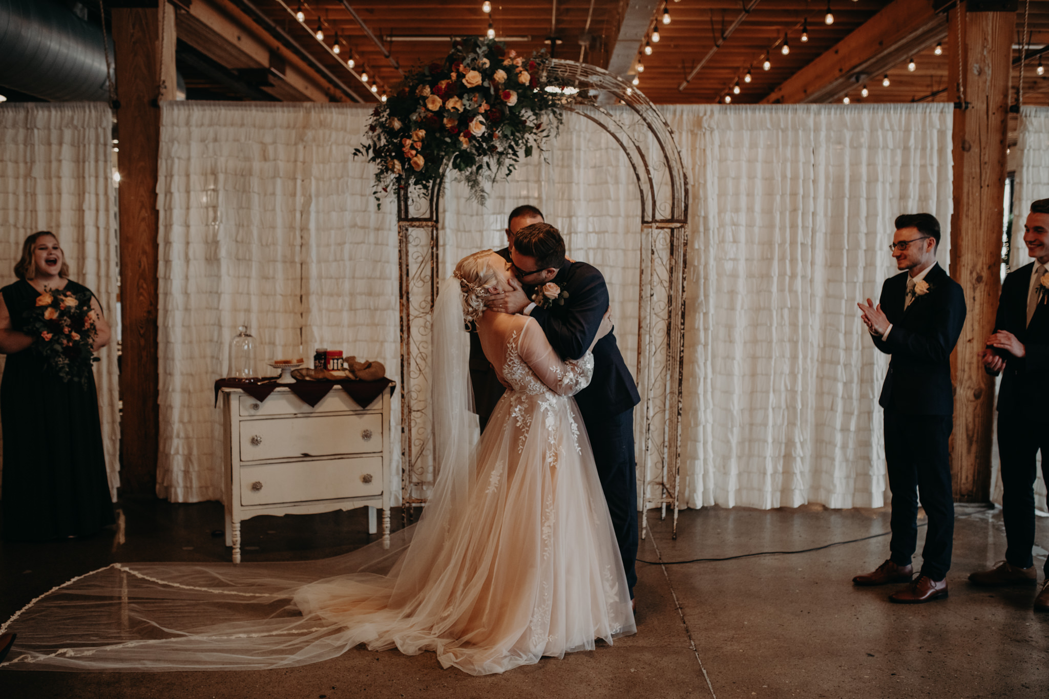 Bride and groom kissing in front of white sheet and an arch at ceremony