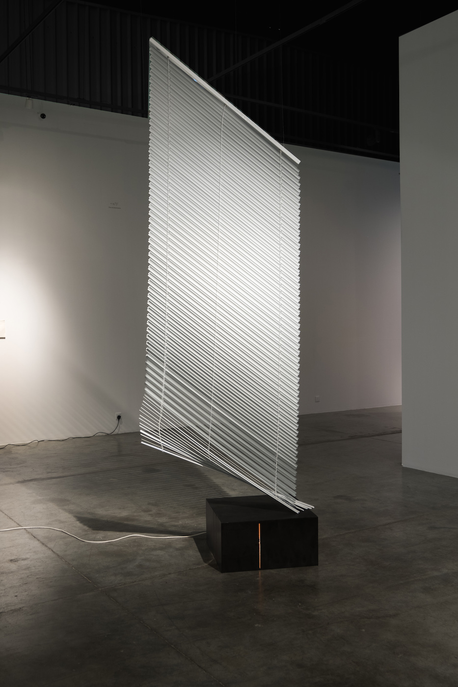  Vittorio Santoro  Good-Bye Darkness, V 2012 Venetian blind (250 x 120 cm), suspension devices, steel wires, black steel base (30 x 60 x 60 cm), light bulb with base, electric cord with plug Dimensions variable  The suspended venetian blind rests par