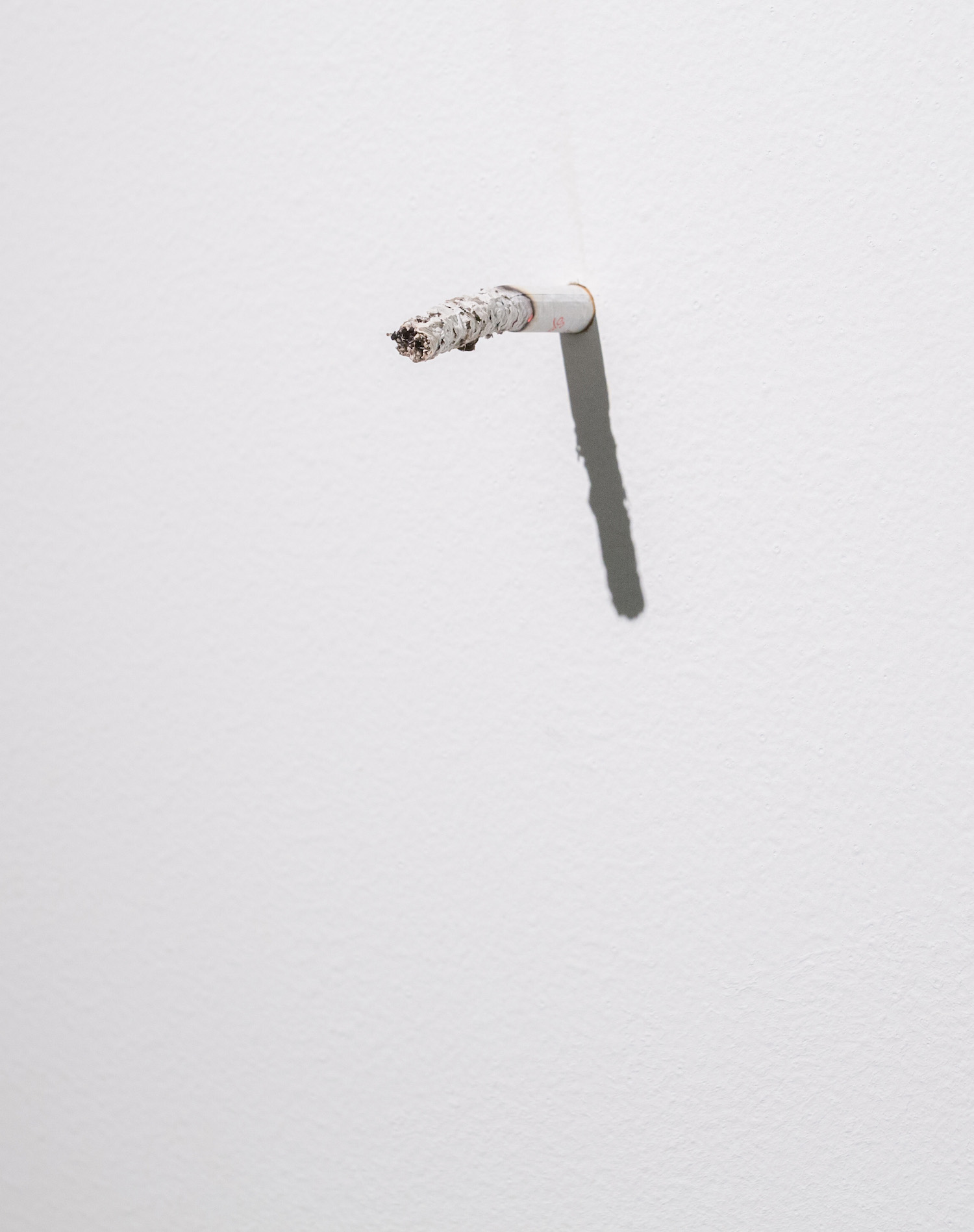  Parler à un mur (detail) 2011 Cigarette Variable dimension  During the exhibition, the gallerist smokes his cigarette with the white wall of the exhibition space. 
