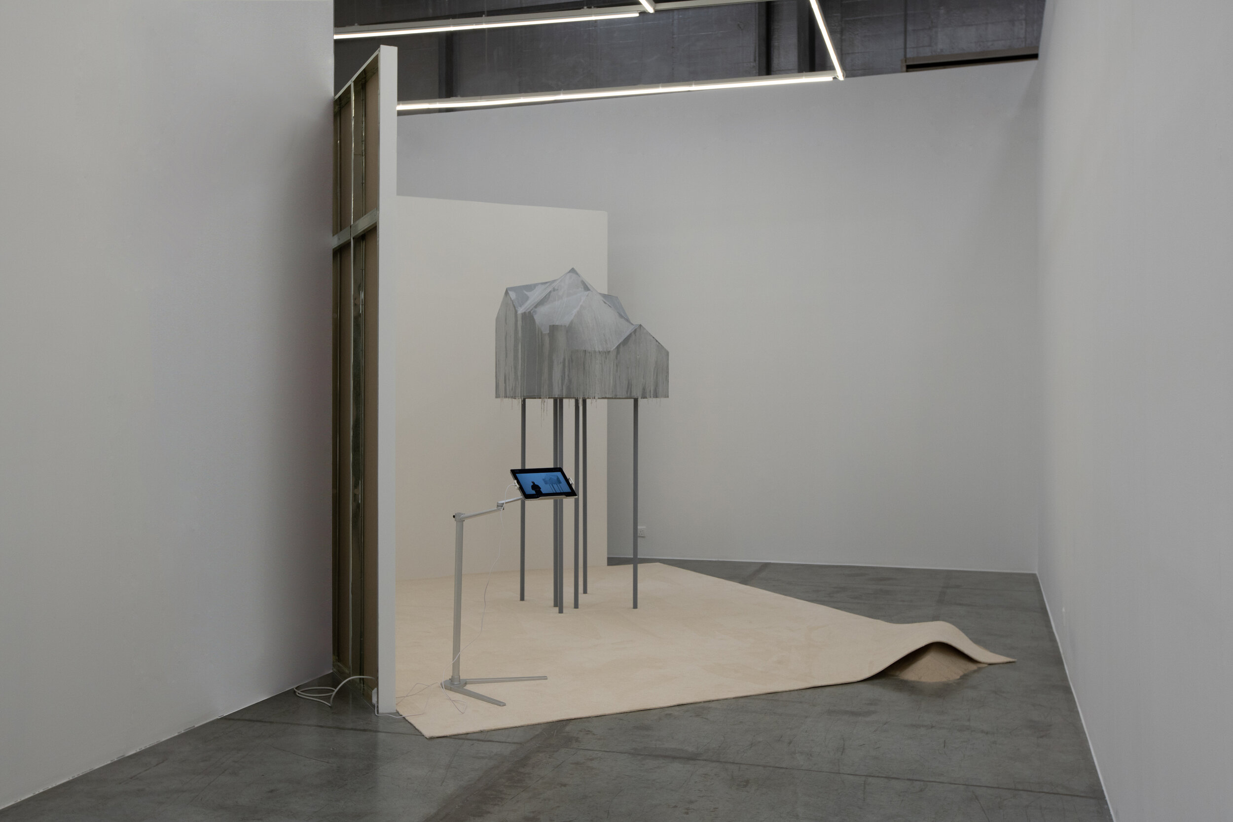  The Booth, The Gallerist and The Mausoleum 2021 Wood, cardboard, votive candles wax, acrylic paint, ashes of press releases, wishes, hopes, metallic structure, carpet, ipad stand, ipad, video 10', desert sand, art fair booth, gallerist, contract Dim