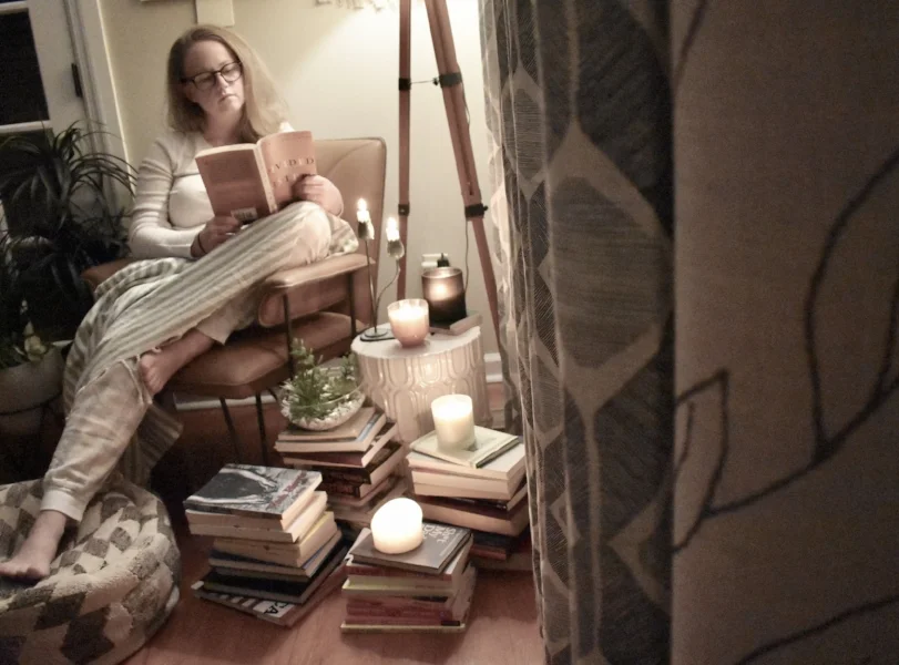 woman in chair reeding book surrounded by books and candles.jpeg