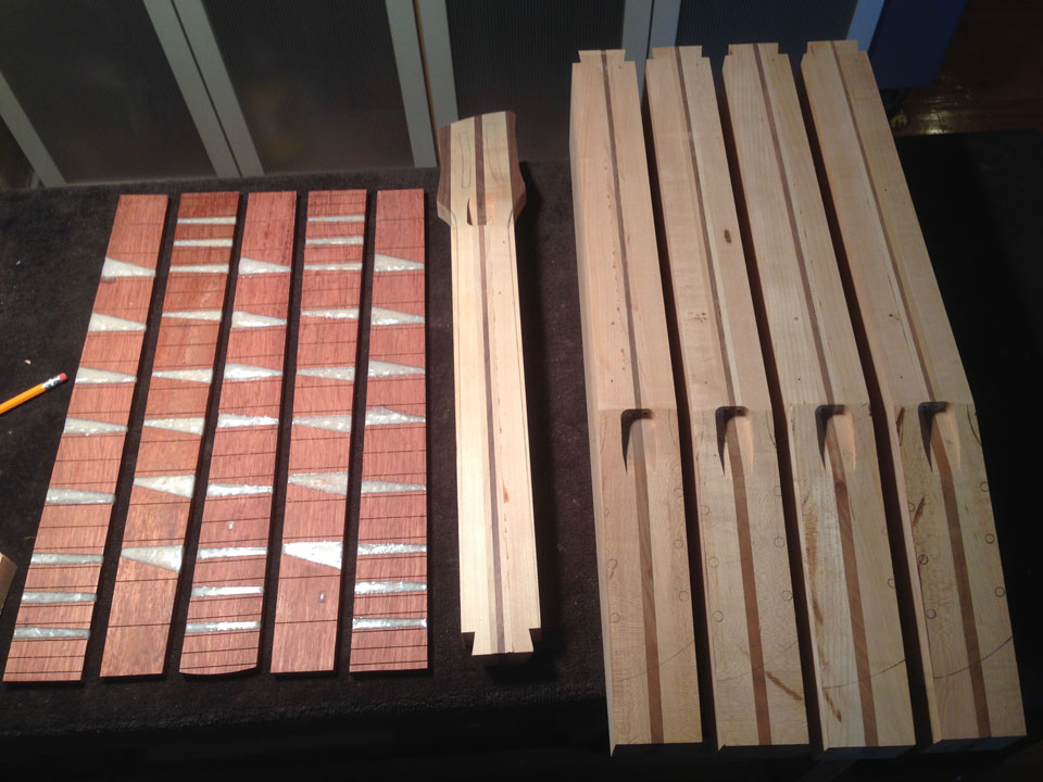 THE COMPONENTS OF SOME NECKS LAID OUT ON THE BENCH: FRETBOARDS, A PARTIALLY-SHAPED NECK, AND ROUGH LAMINATED NECK BLOCKS THAT HAVEN'T BEEN TRIMMED OR SHAPED YET.