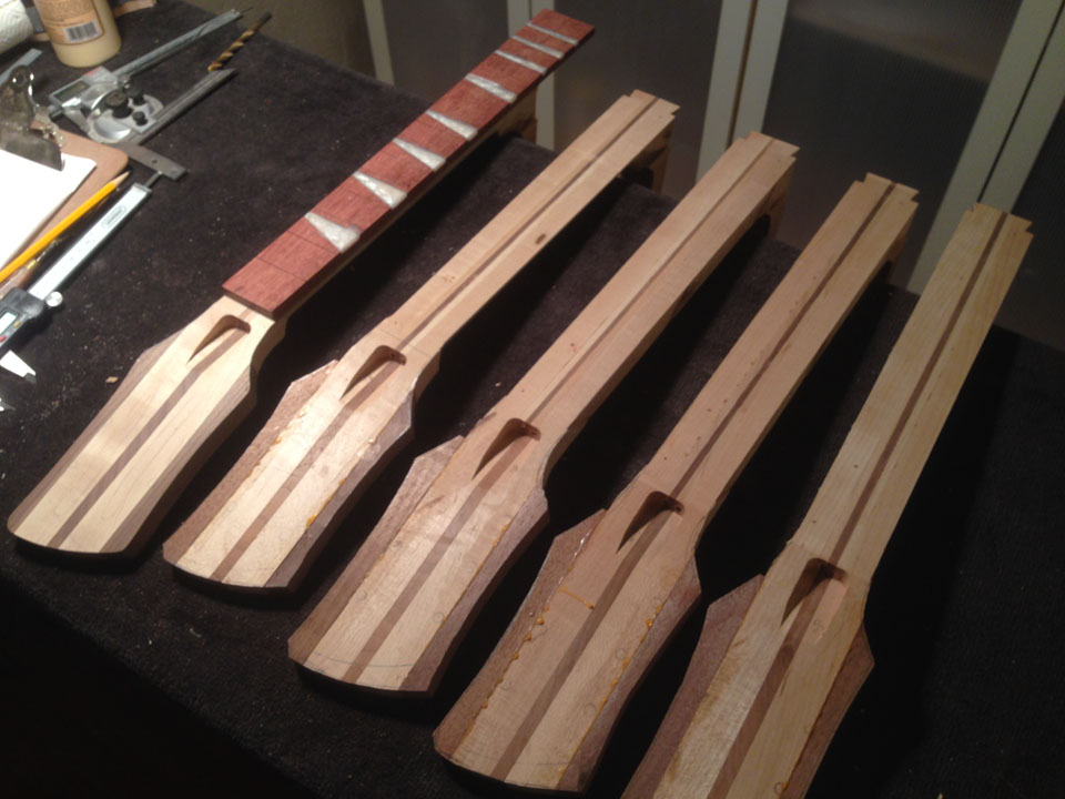 NECKS HAVE THEIR TRUSS ROD CHANNELS AND ADJUSTMENT POCKETS IN PLACE. NOTE HOW THE FRETBOARD OVERHANGS THE NECK HEEL. IT'S GLUED TO THE TOP OF THE BODY.