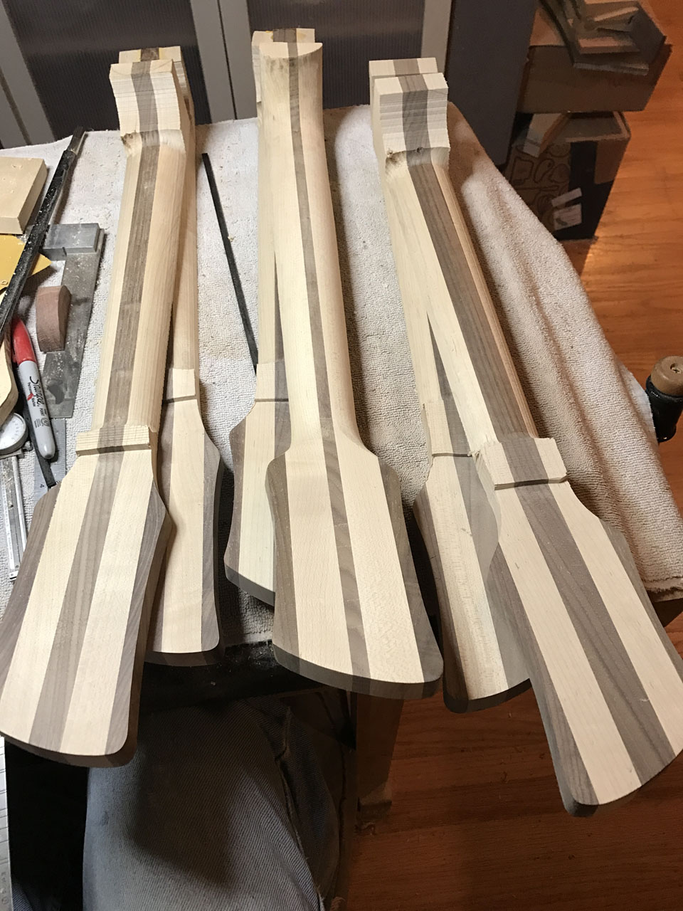 NECKS IN VARIOUS STAGES ON SHAPING. THE CENTER NECK IS READY FOR FINE-SANDING AND DRILLING FOR TUNERS.