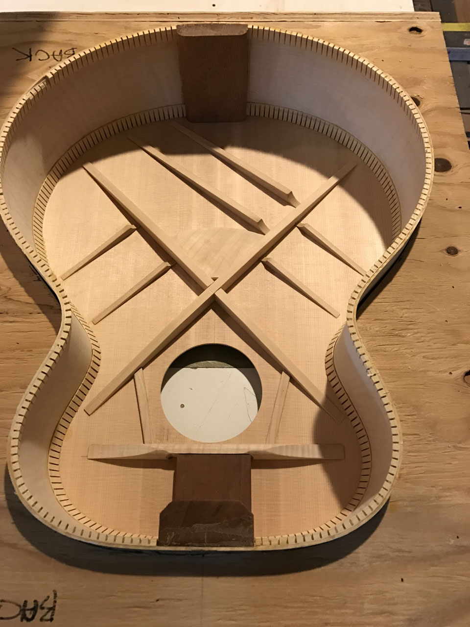 LOOKING AT THE INSIDE OF A JUMBO BODY WITH THE TOP GLUED INTO PLACE. BRIDGE PLATE HAS BEEN FITTED BELOW THE "X" BRACE. SOUND HOLE ON THIS ONE HAS NOT BEEN BOUND YET.