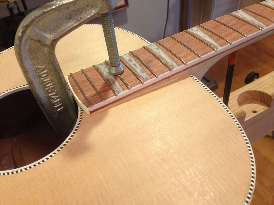 UPON GLUING, THE NECK IS CLAMPED IN TWO PLANES: DOWN ONTO THE BODY AND TO THE TOP, AND WITH A STRAP CLAMP TO FASTEN IT TO THE NECK HEEL BLOCK FOR A SOLID ANCHOR POINT.