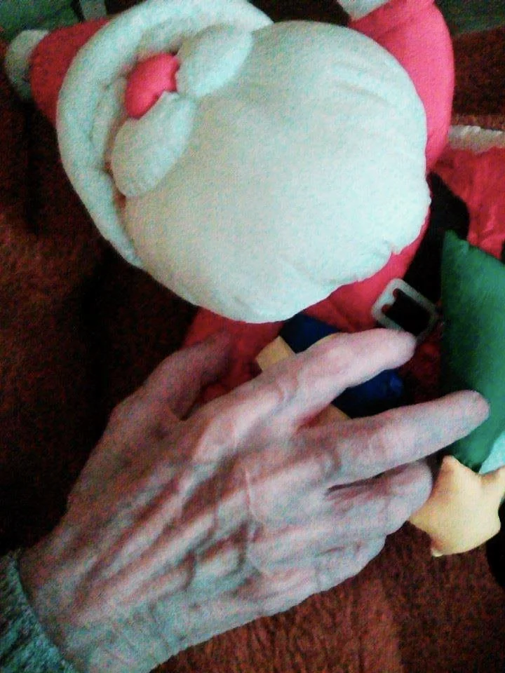 Das Bild zeigt die Hand einer Bewohnerin eines Altenheimes mit einer Weihnachtsmannpuppe.