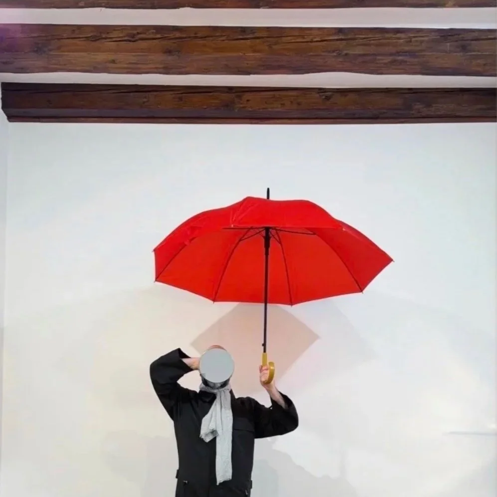Person holding a red umbrella in front of a plain wall with wooden beams above.