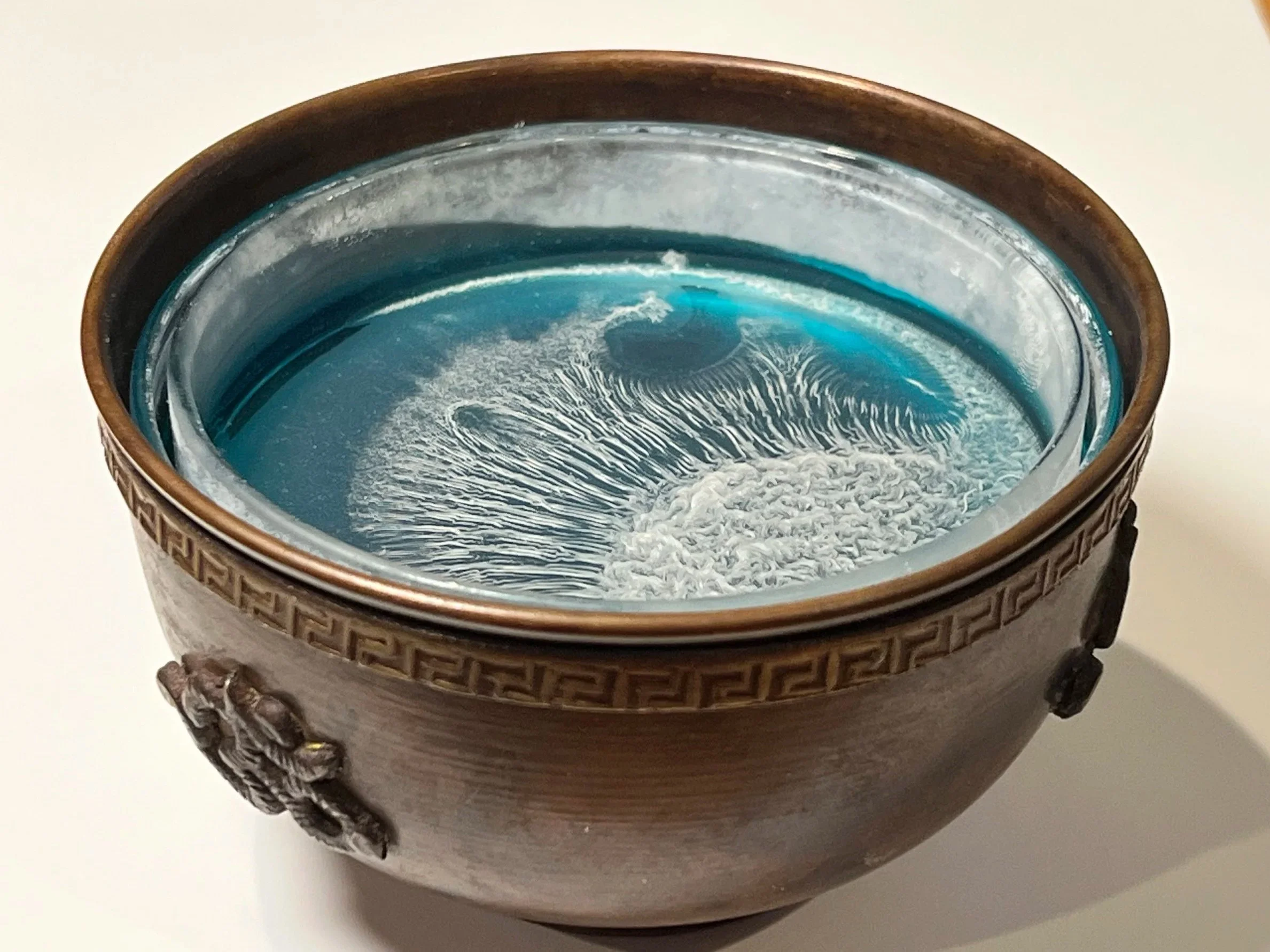 A decorative brown vase with a Greek key pattern around the top contains water with a floating glass clock.