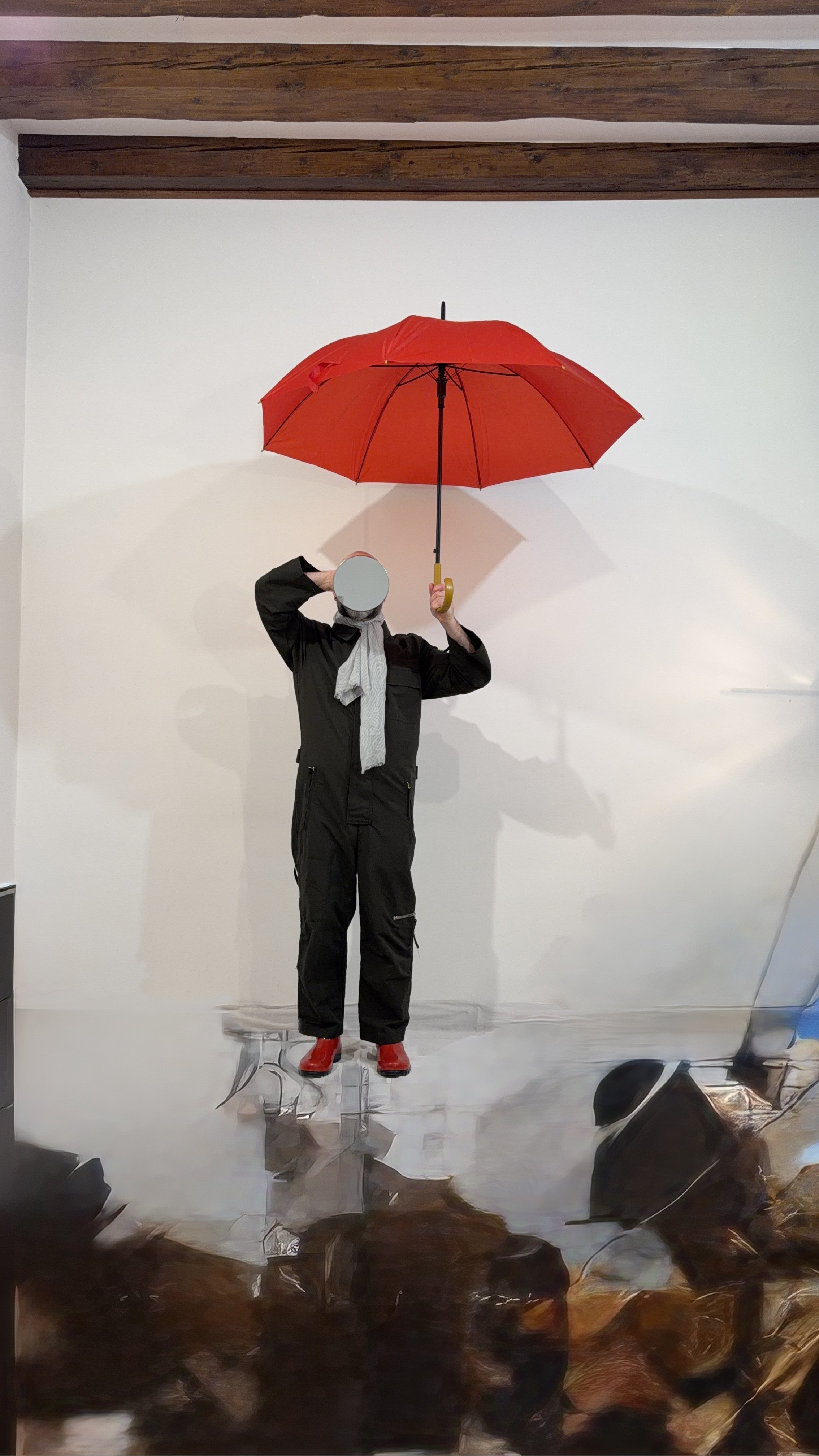 Art installation of a mannequin holding a red umbrella, standing on a reflective floor, with an audience visible in the foreground.