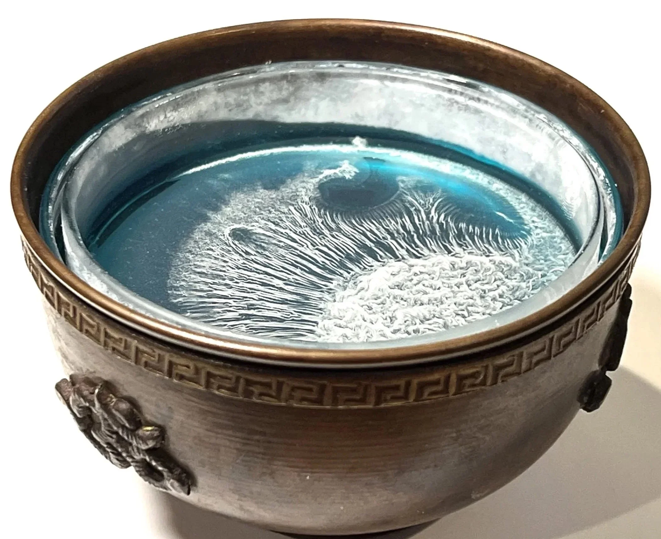 A decorative ceramic or metal vase with a textured pattern on the exterior, filled with water or a reflective liquid, showing a swirling pattern on the surface.