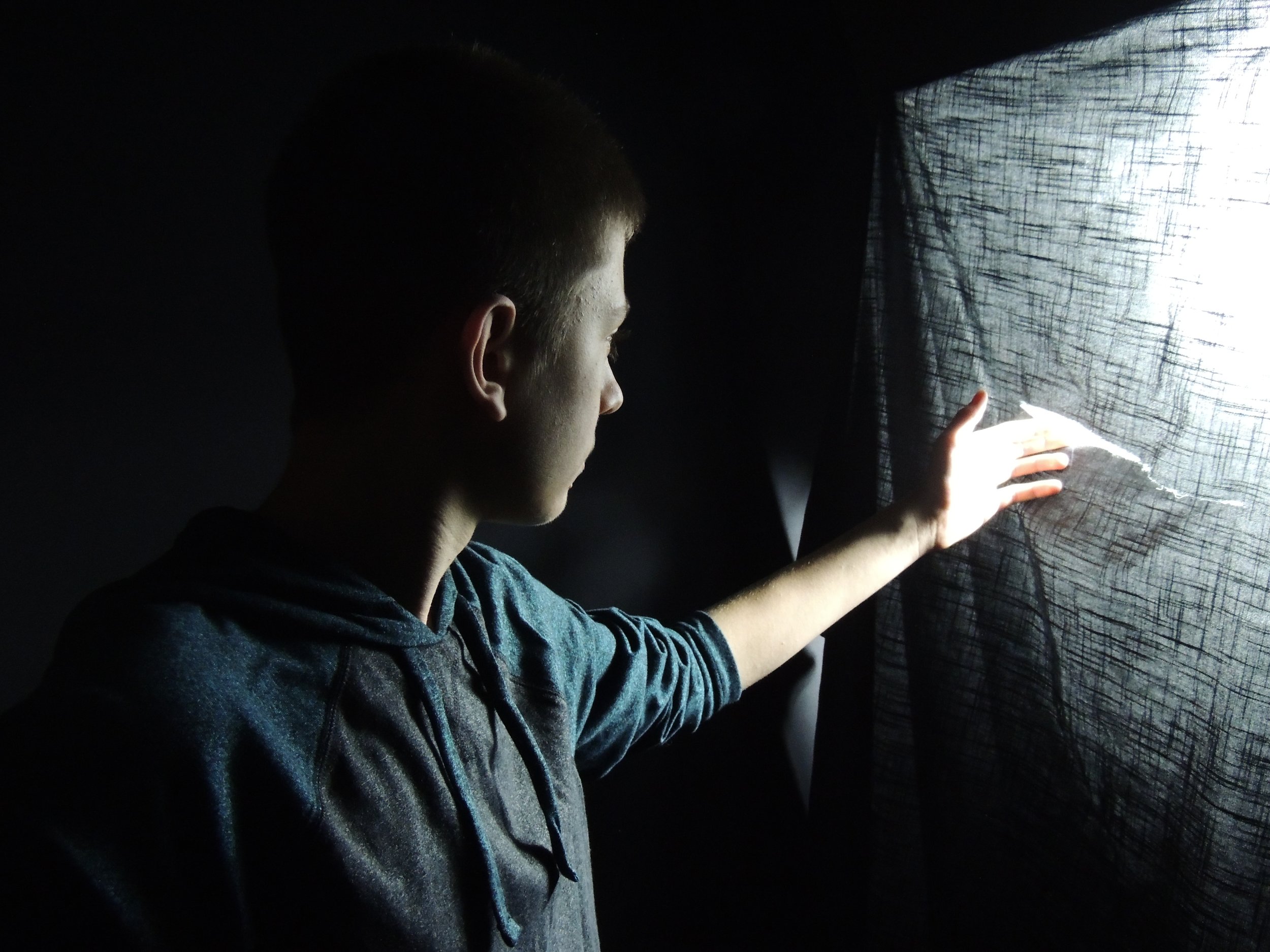 Boy looking at light through tear in sheet