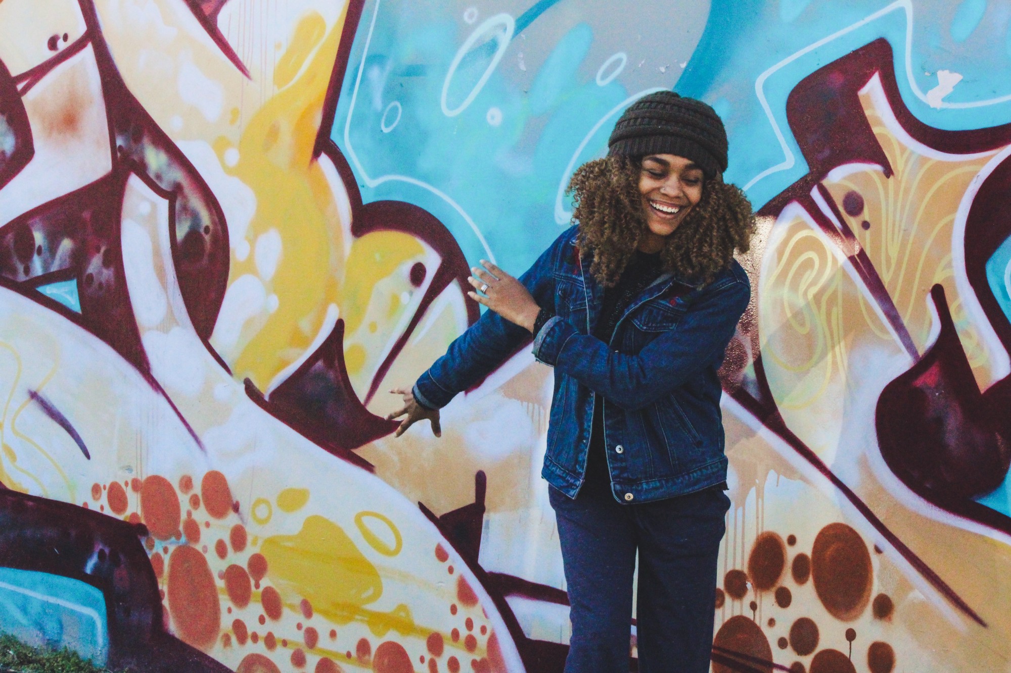 African American woman smiling and dancing in front of a large graffiti mural
