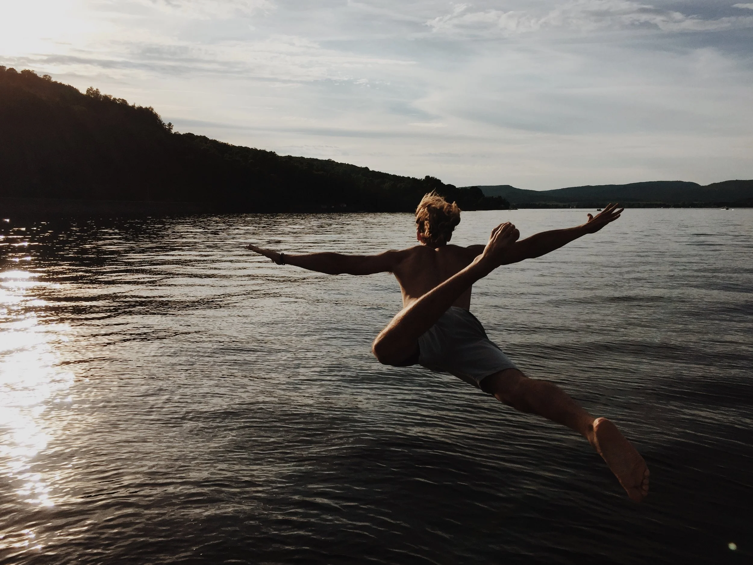 man in bathing suit jumping into lake with arms stretched out like an airplane