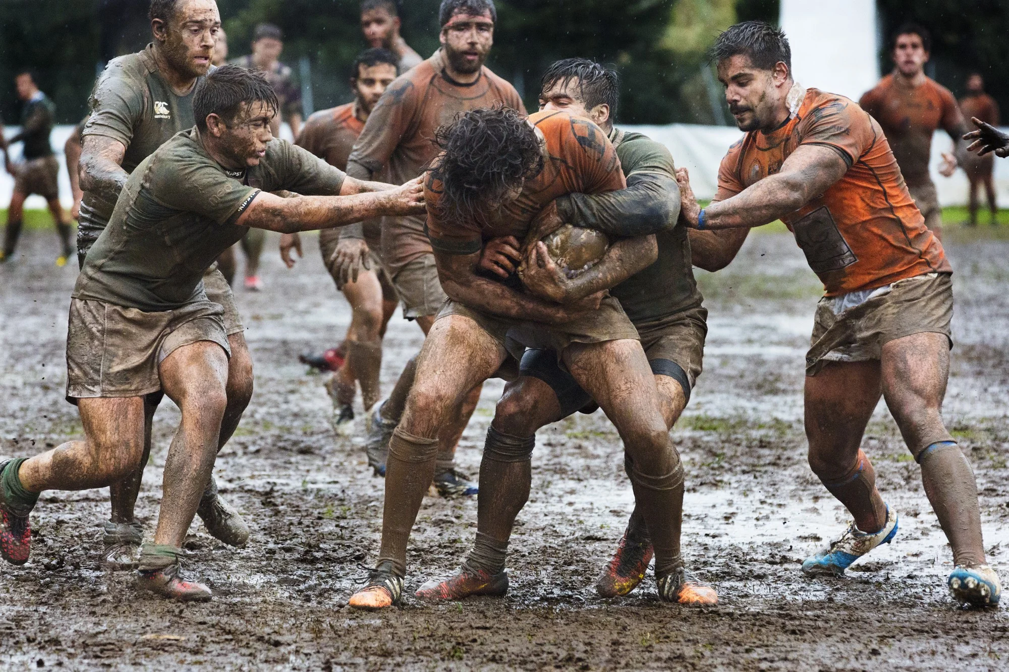 strong men playing rugby in muddy field