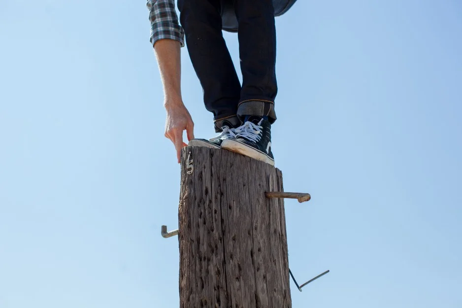 man balancing himself on top of telephone pole