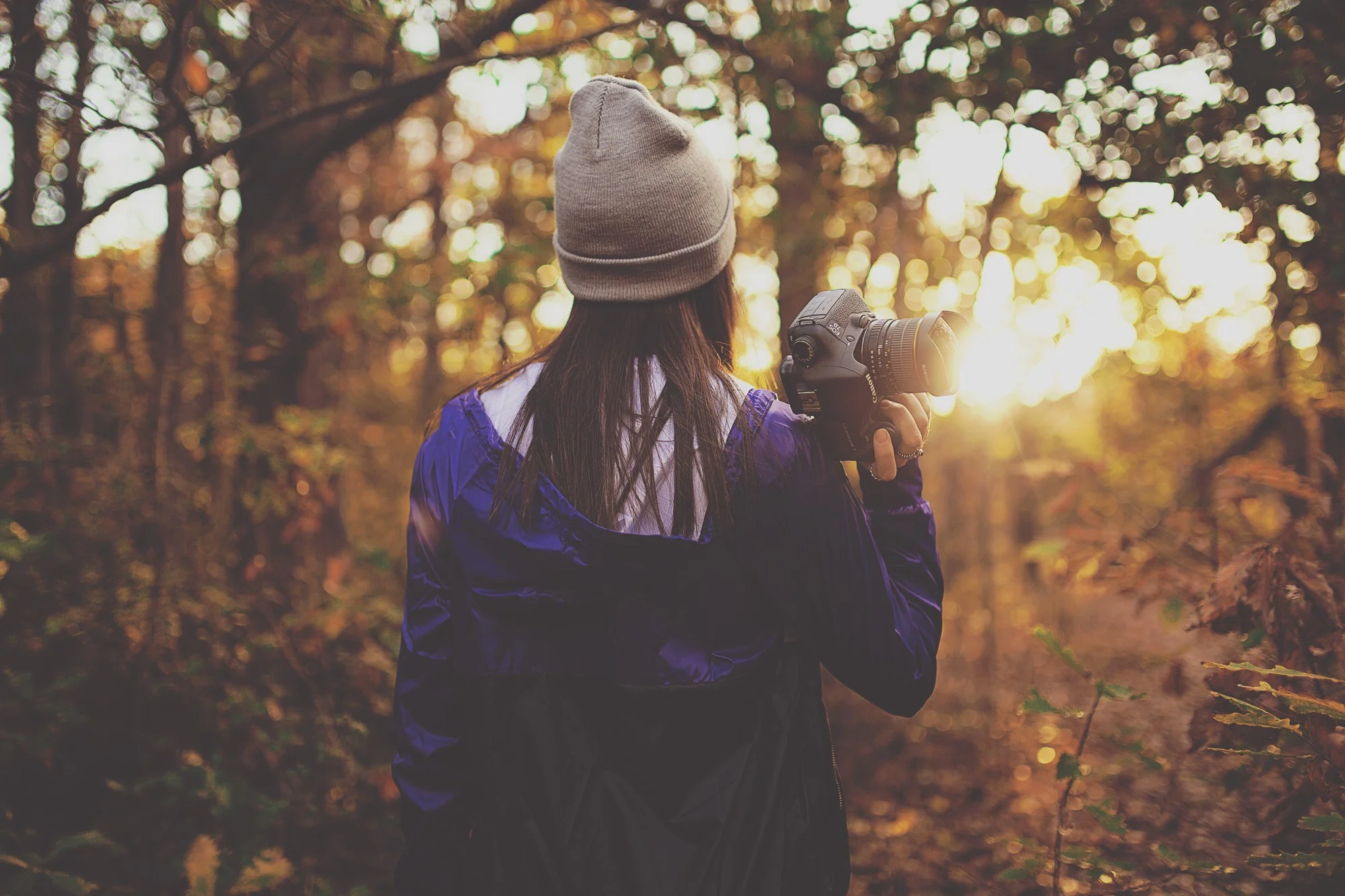 woman holding camera facing sun shining through trees