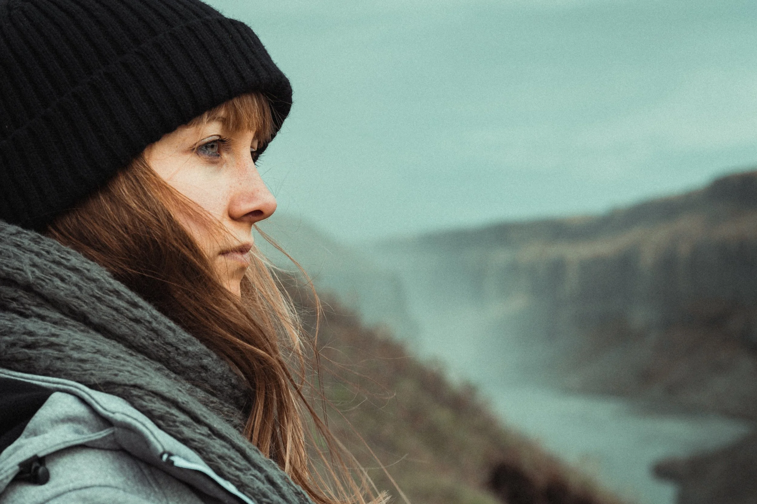 anxious woman dressed for winter staring into distance with river in background