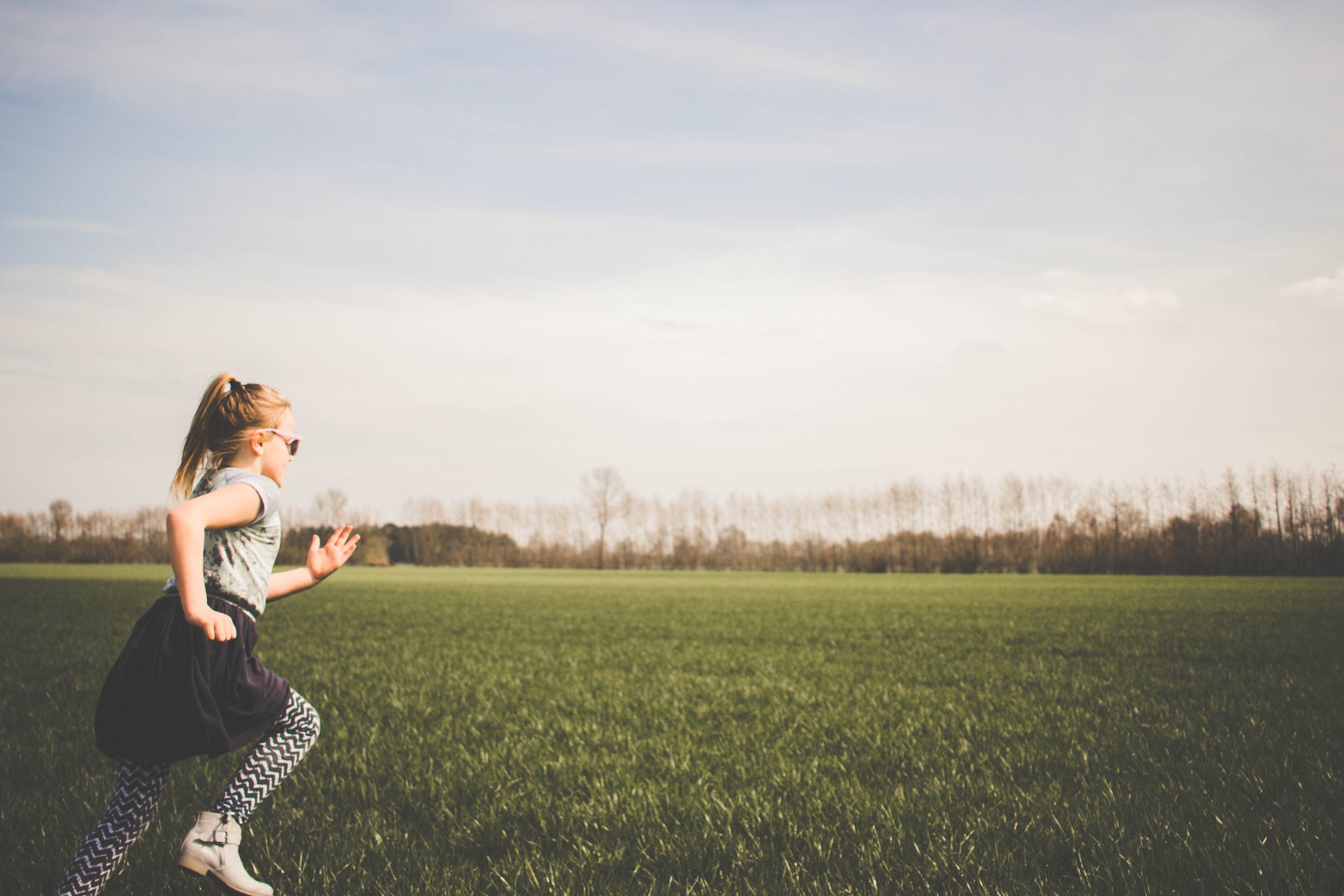 adolescent girl running across grass field