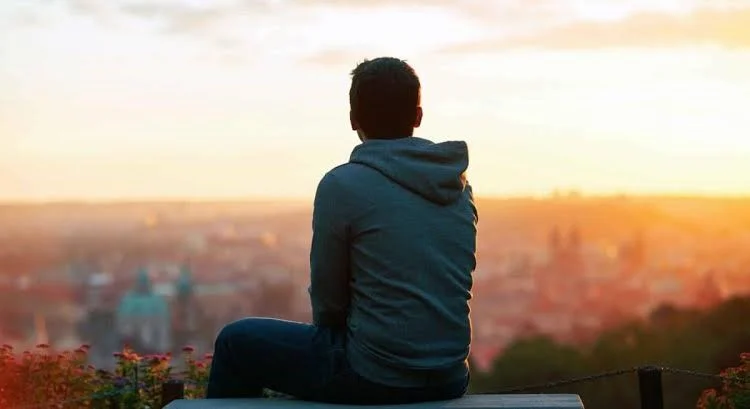 teenager boy sitting on ledge looking at city skyline