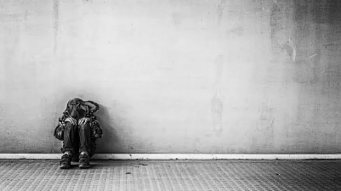 depressed boy sitting with back against concrete wall