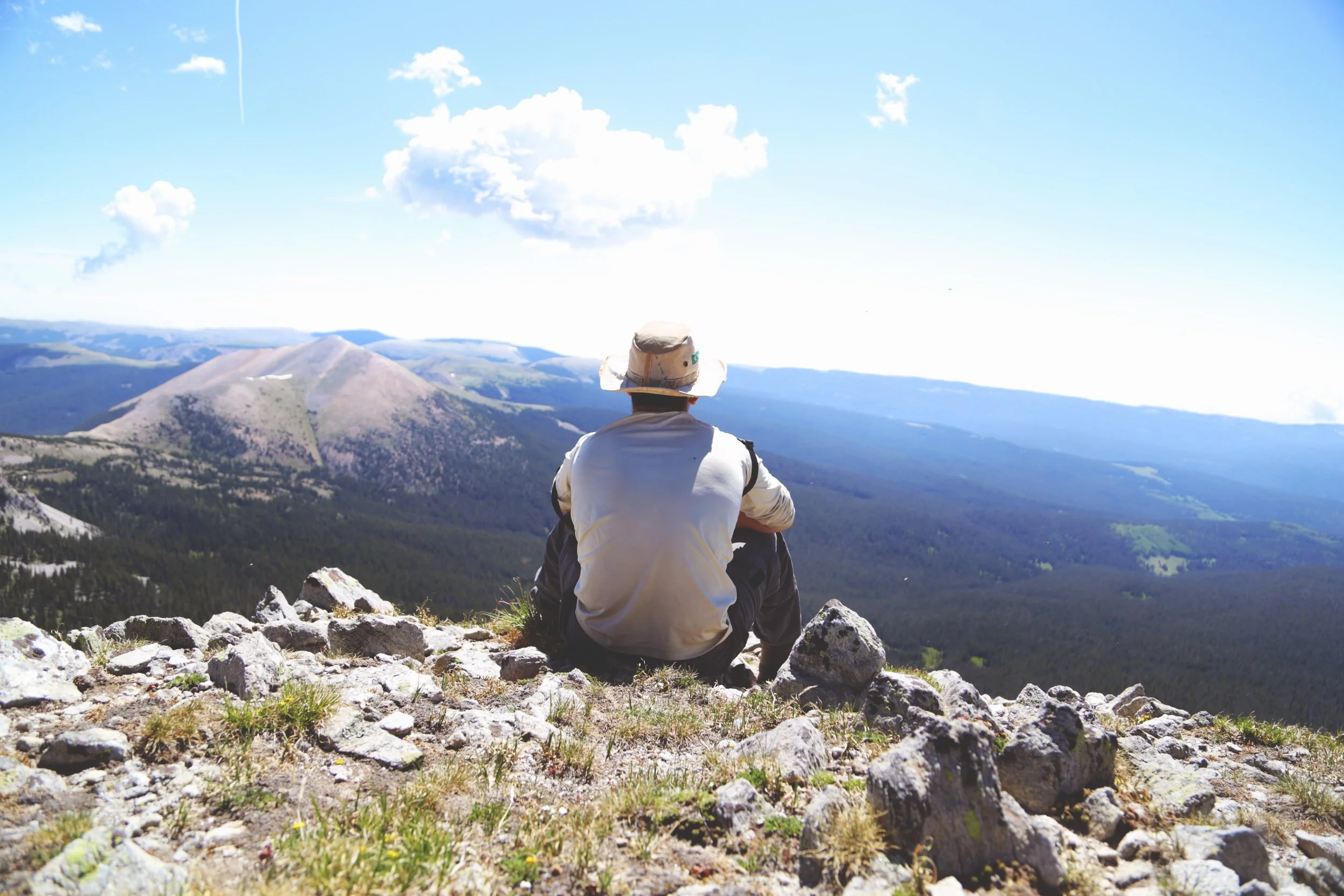 man sitting on mountain summit looking at landscape