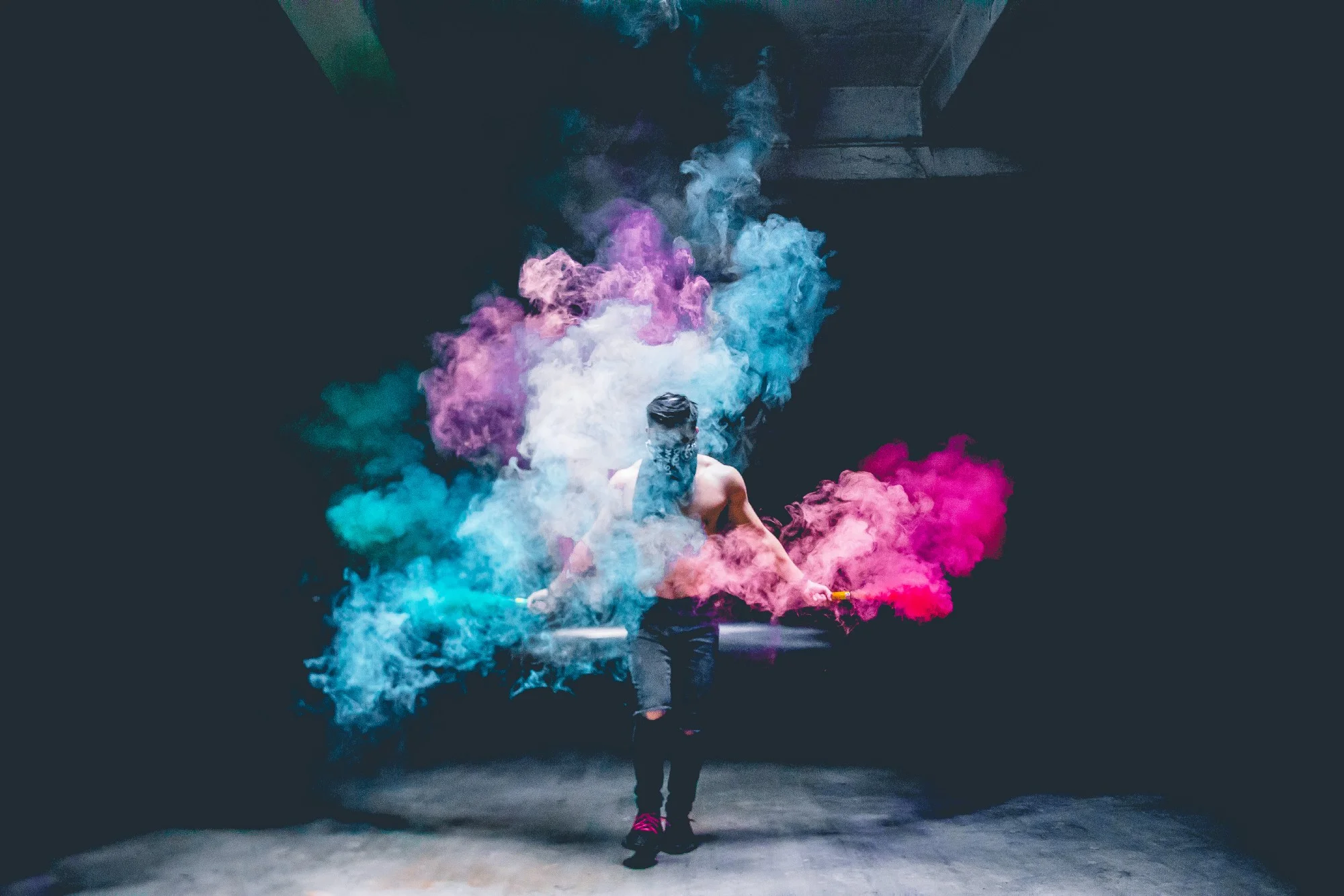 shirtless man wearing bandanna spraying colored smoke