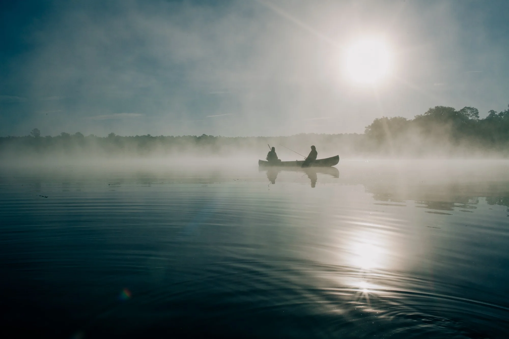 two people rowing through mist on a lake