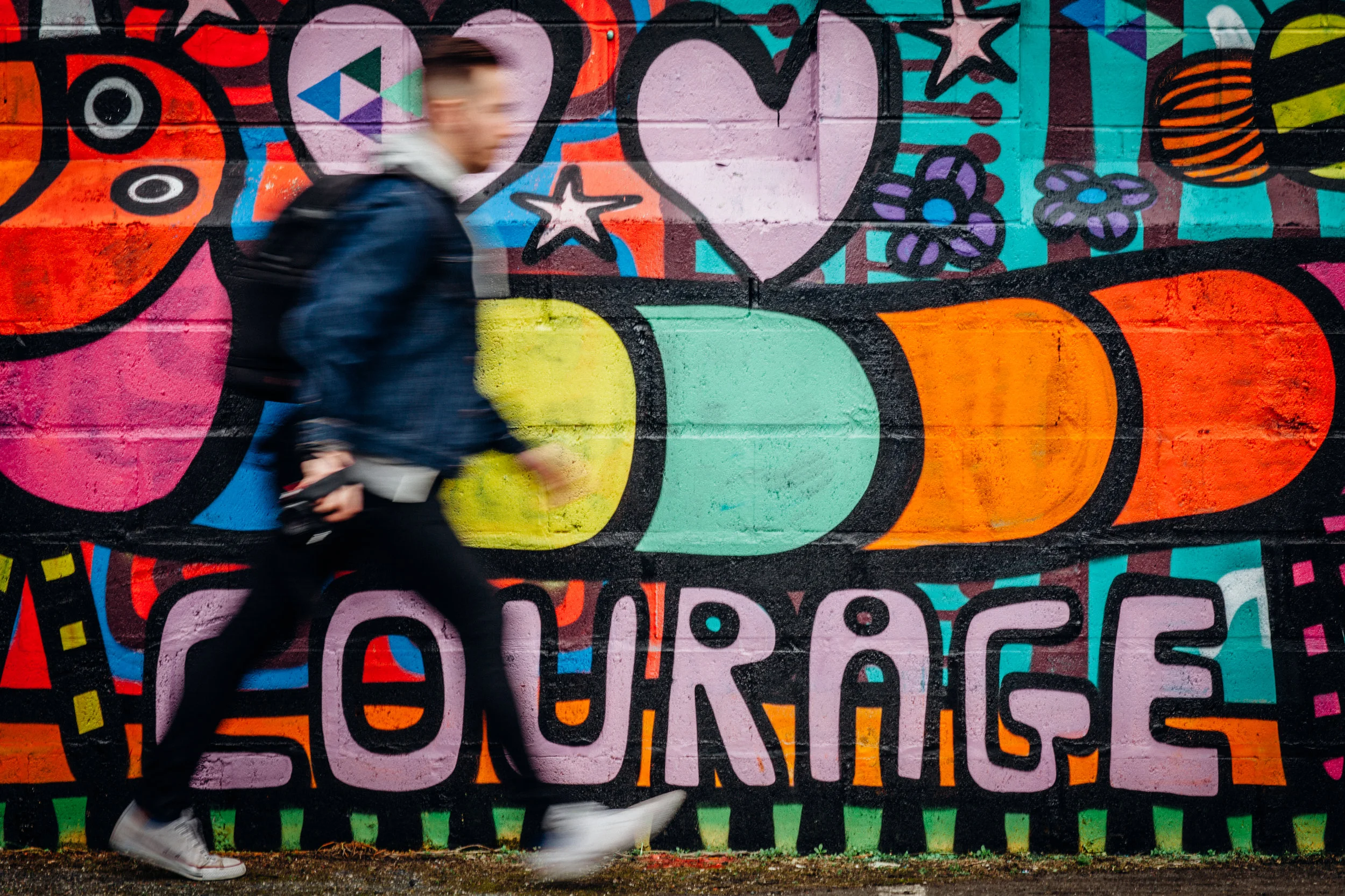 mentally healthy man walking past mural of the word courage